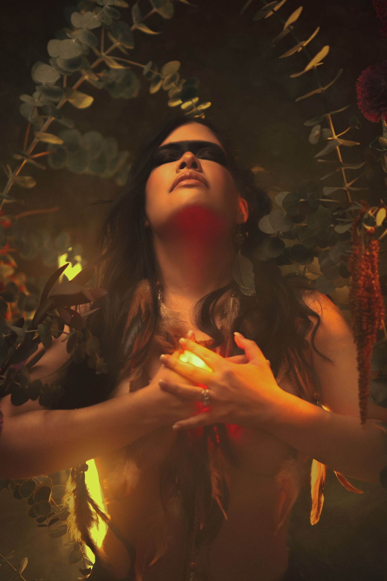 Ethereal portrait surrounded by leaves and warm glowing light in dark setting.
