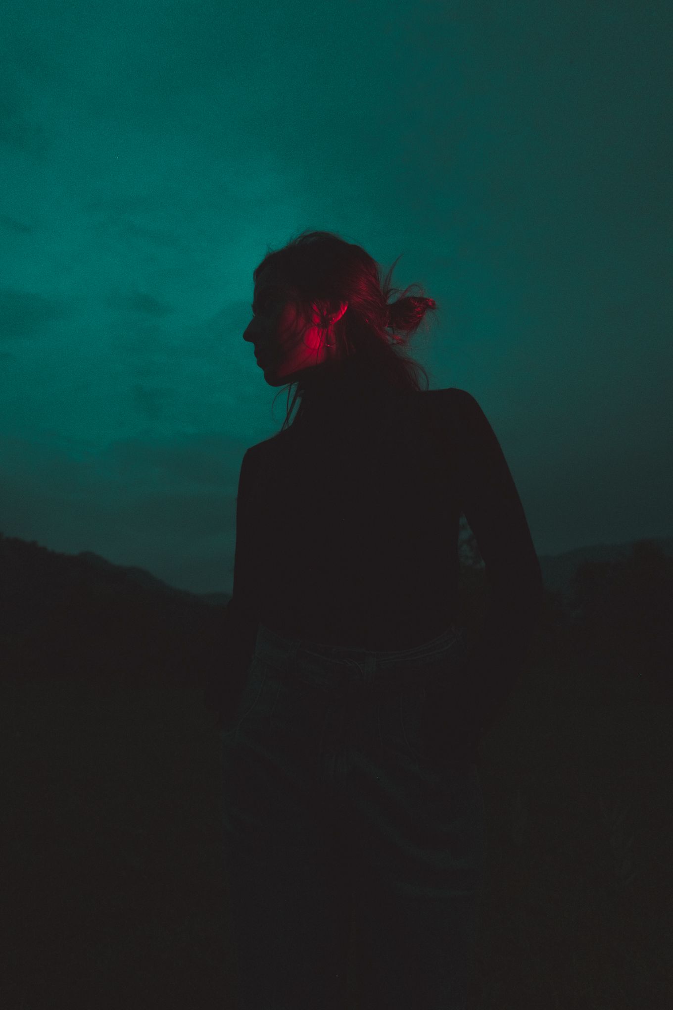 Dark silhouette figure against teal sky with red accent lighting.