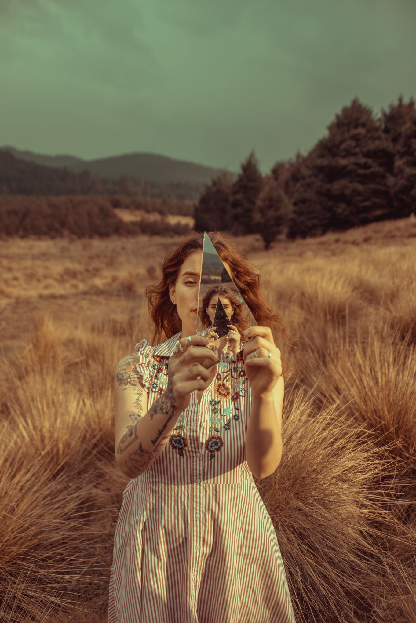Whimsical portrait holding triangular mirror in field of tall grass.