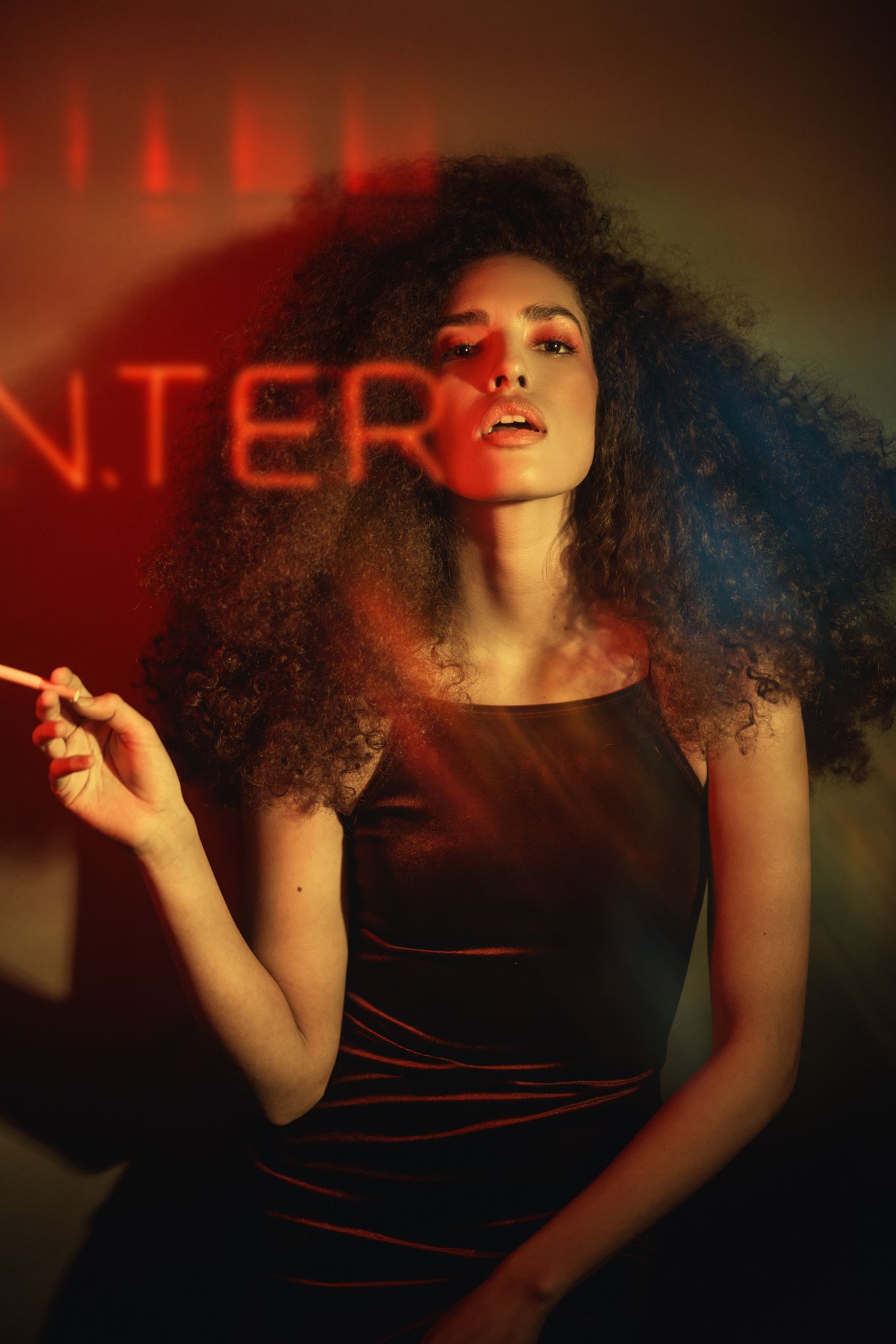 Portrait under red neon lighting with curly hair and black outfit.