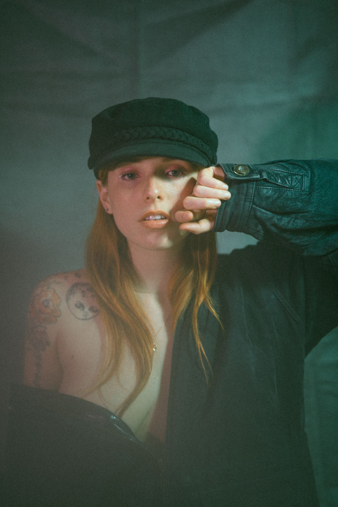 Vintage-styled portrait with newsboy cap and dramatic teal lighting.