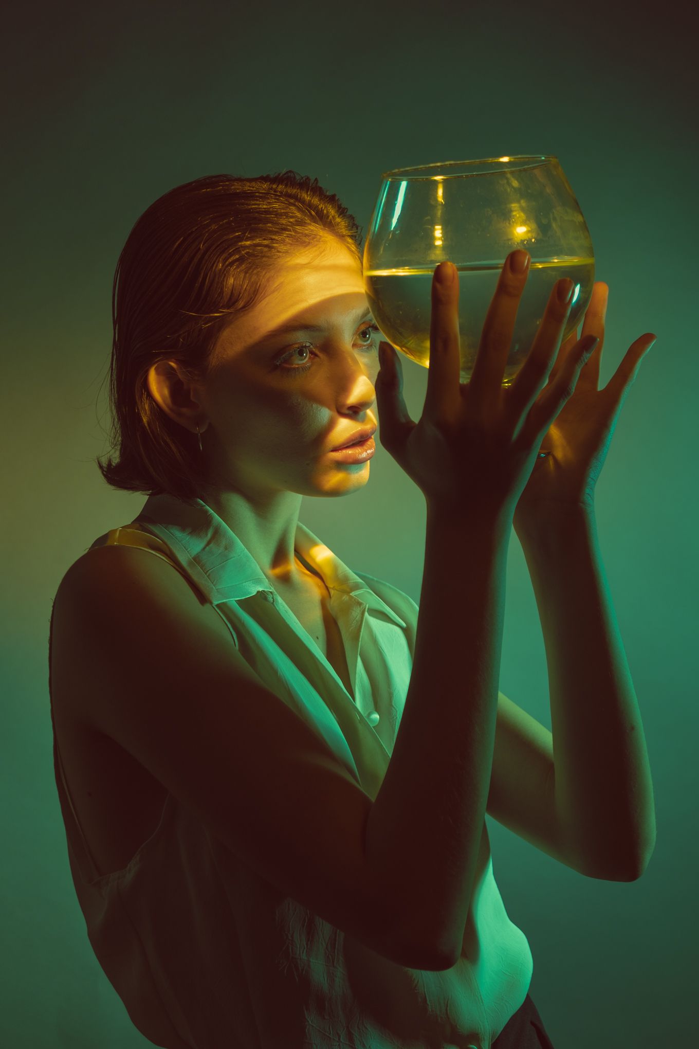 Dramatic portrait with subject gazing through wine glass in ethereal green lighting.