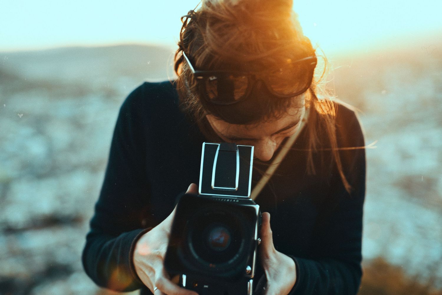 Photographer holding vintage camera at sunset with sun flare in background.