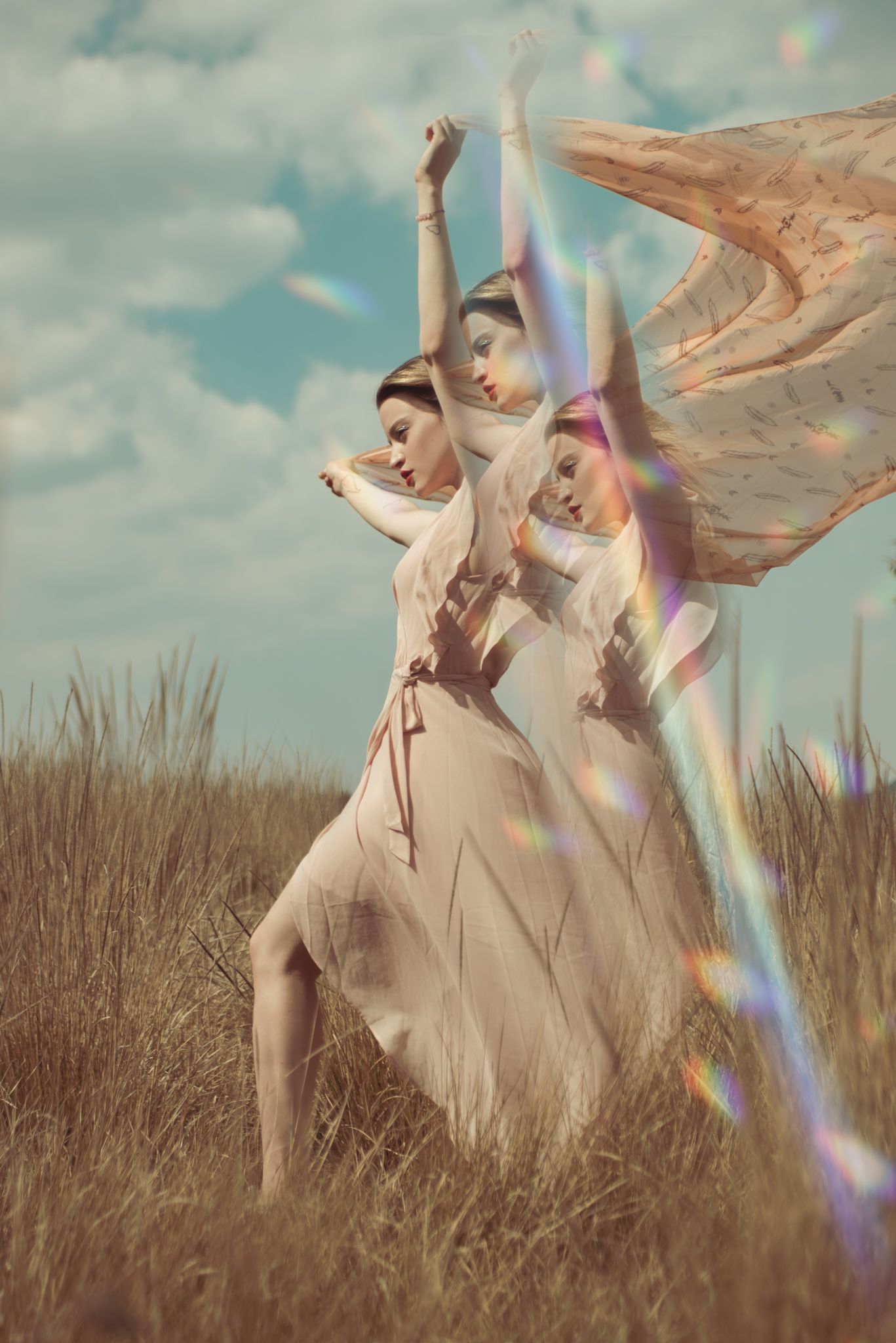 Three dancers in flowing white dresses perform in a sunlit field with lens flare effects.