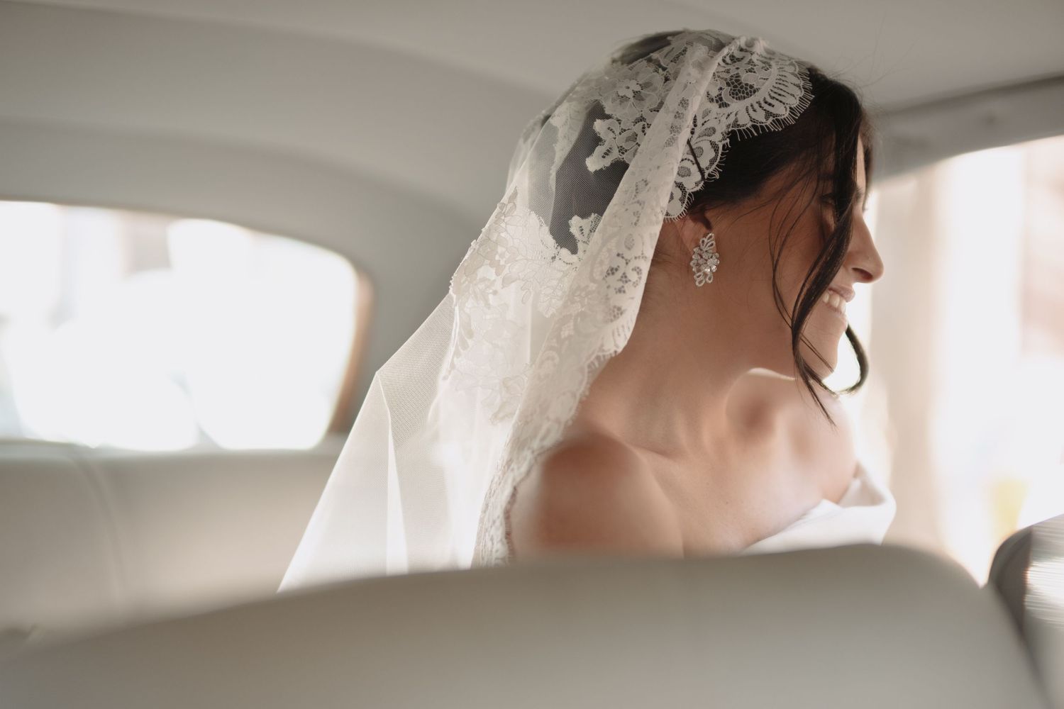 Elegant side profile view of bride wearing traditional lace veil in car backseat.