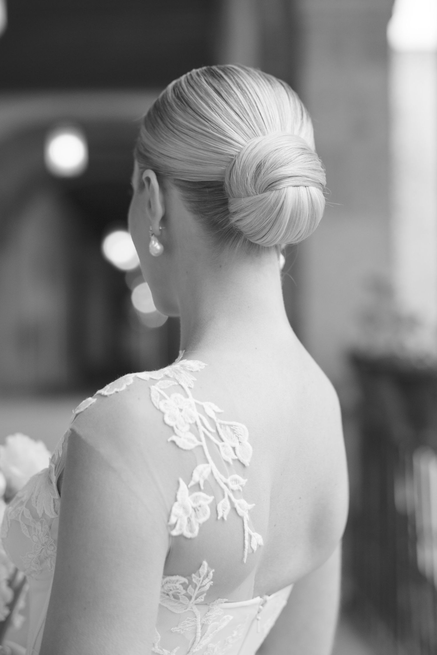 Elegant bridal updo hairstyle with lace detail on wedding dress shown from behind.
