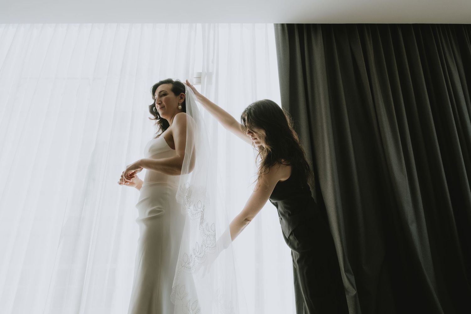 Wedding preparation scene with elegant dress fitting in natural window light.