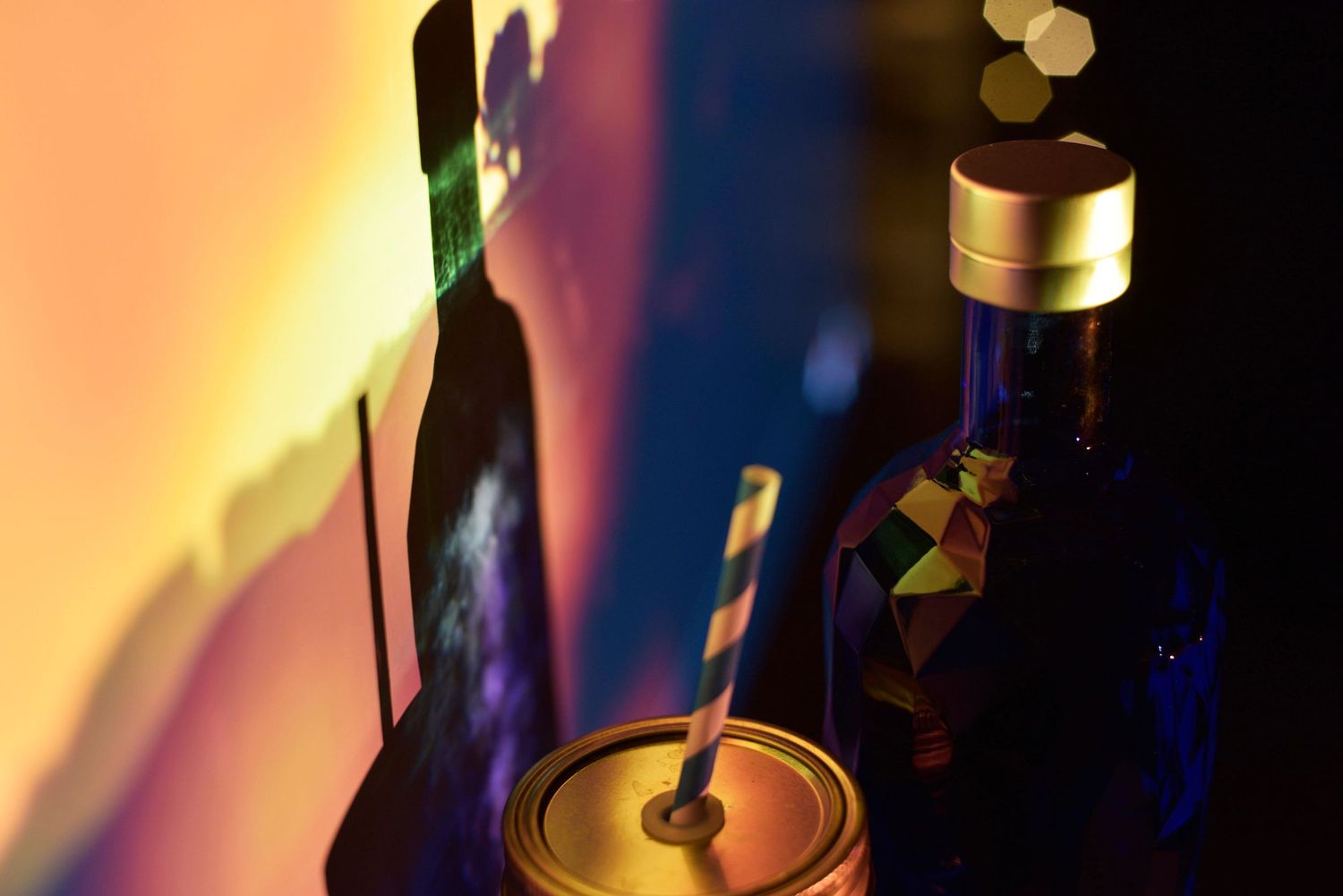 Multi-colored bokeh lights create a blurry, abstract background with dark silhouettes of bottles in the foreground.