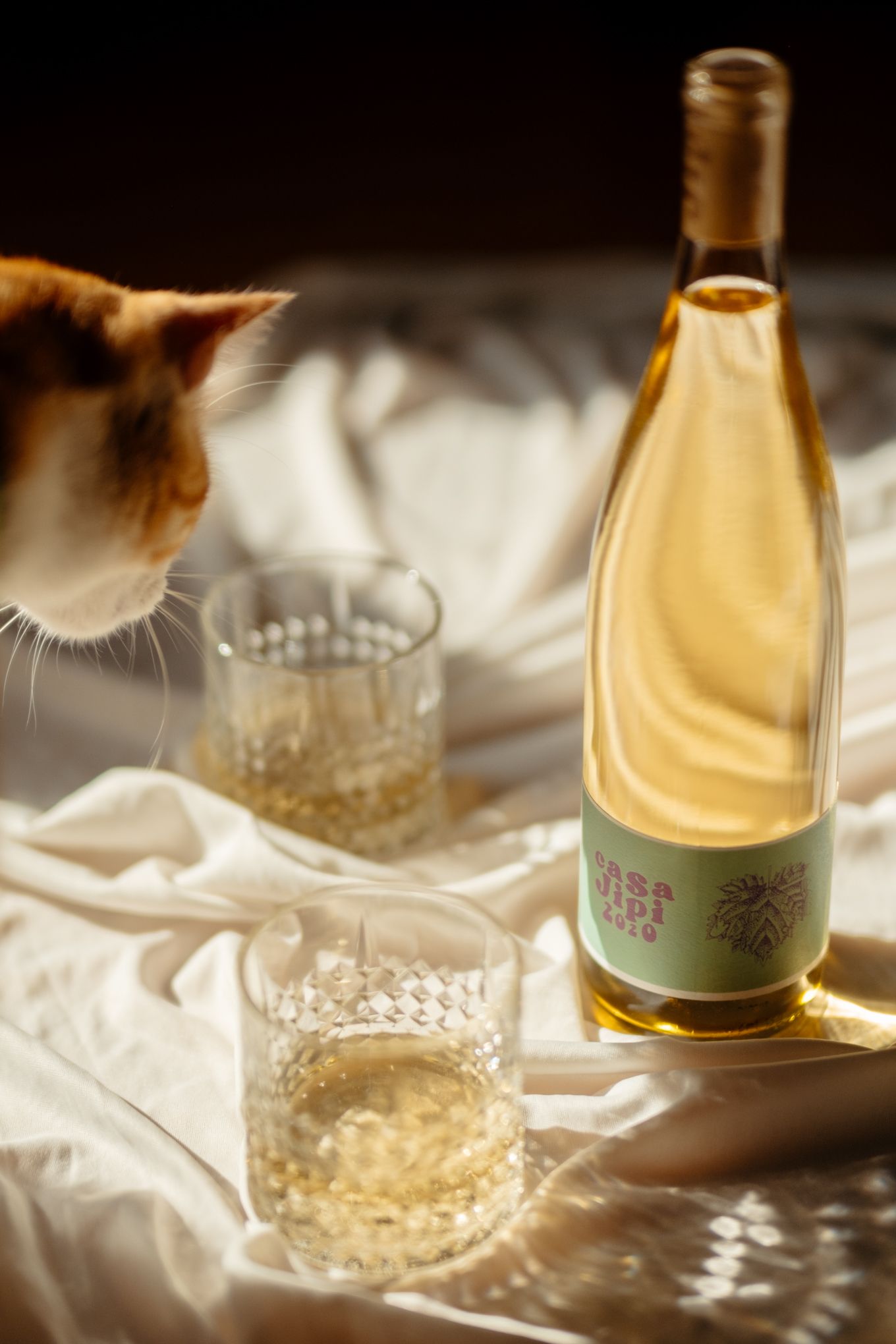An artistic composition of a wine bottle and vintage cut crystal glass on white linen with natural lighting.