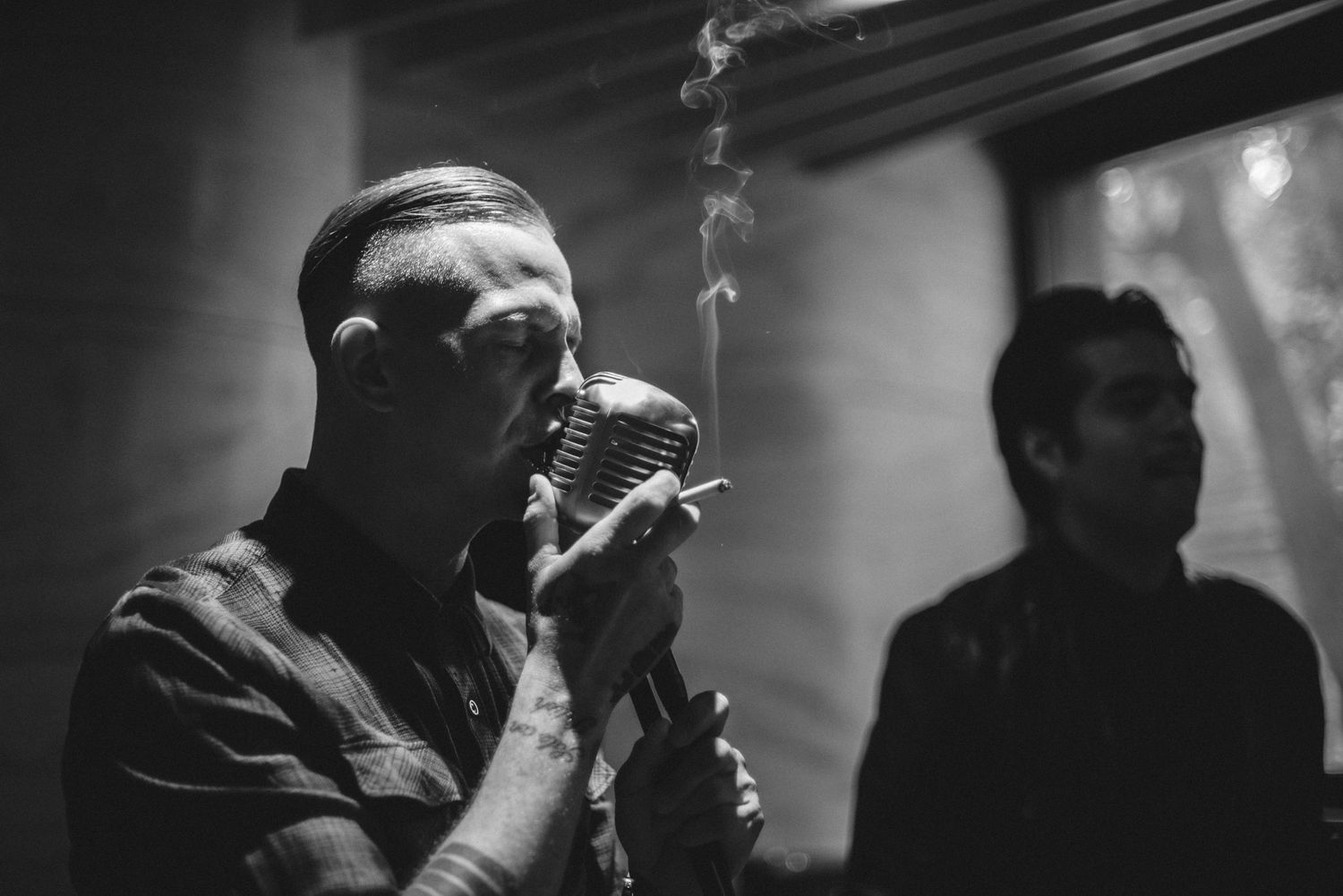 Moody black and white photo of a singer performing with smoke effects and microphone.