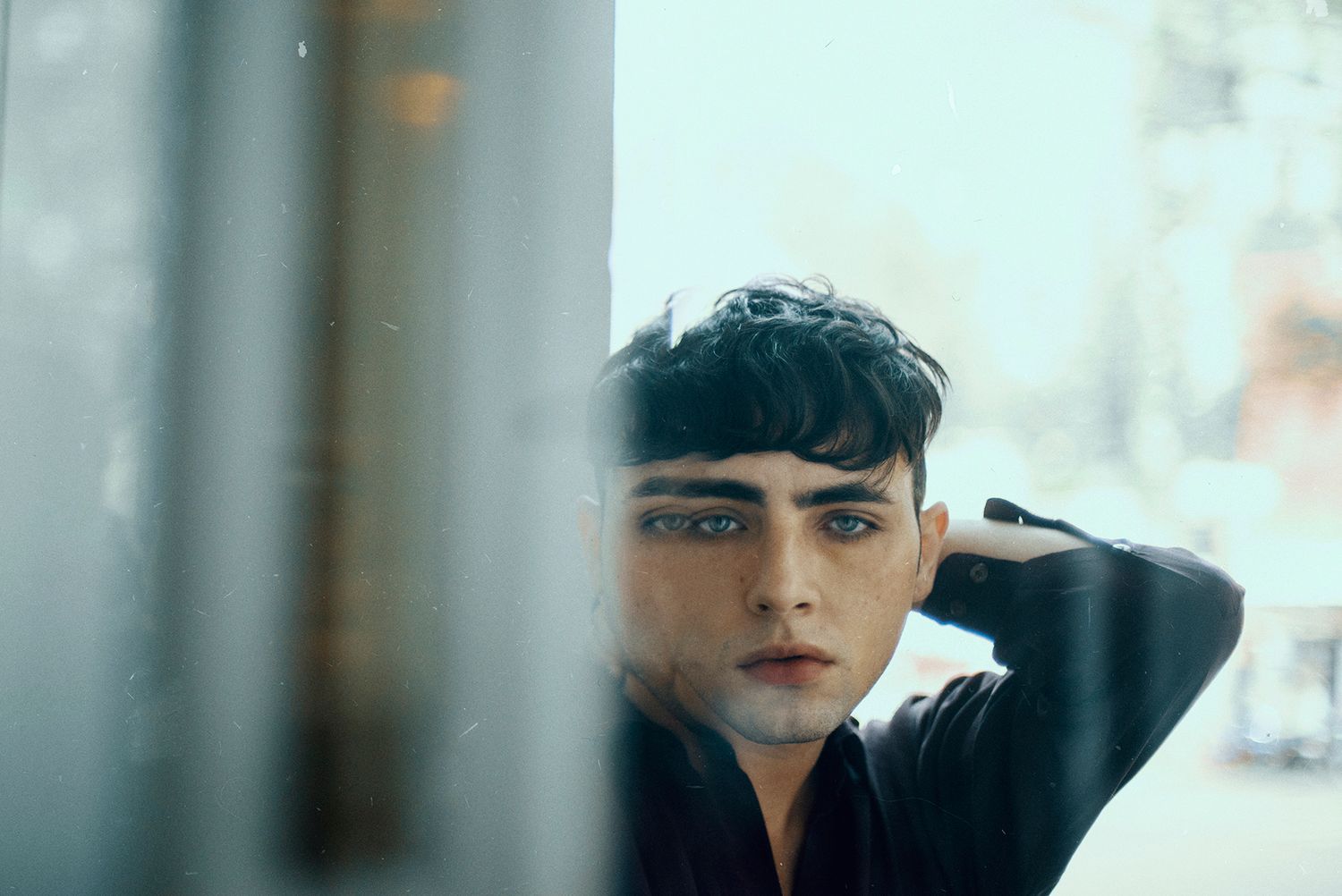 Close-up portrait through window glass creating dreamy, reflective atmosphere.