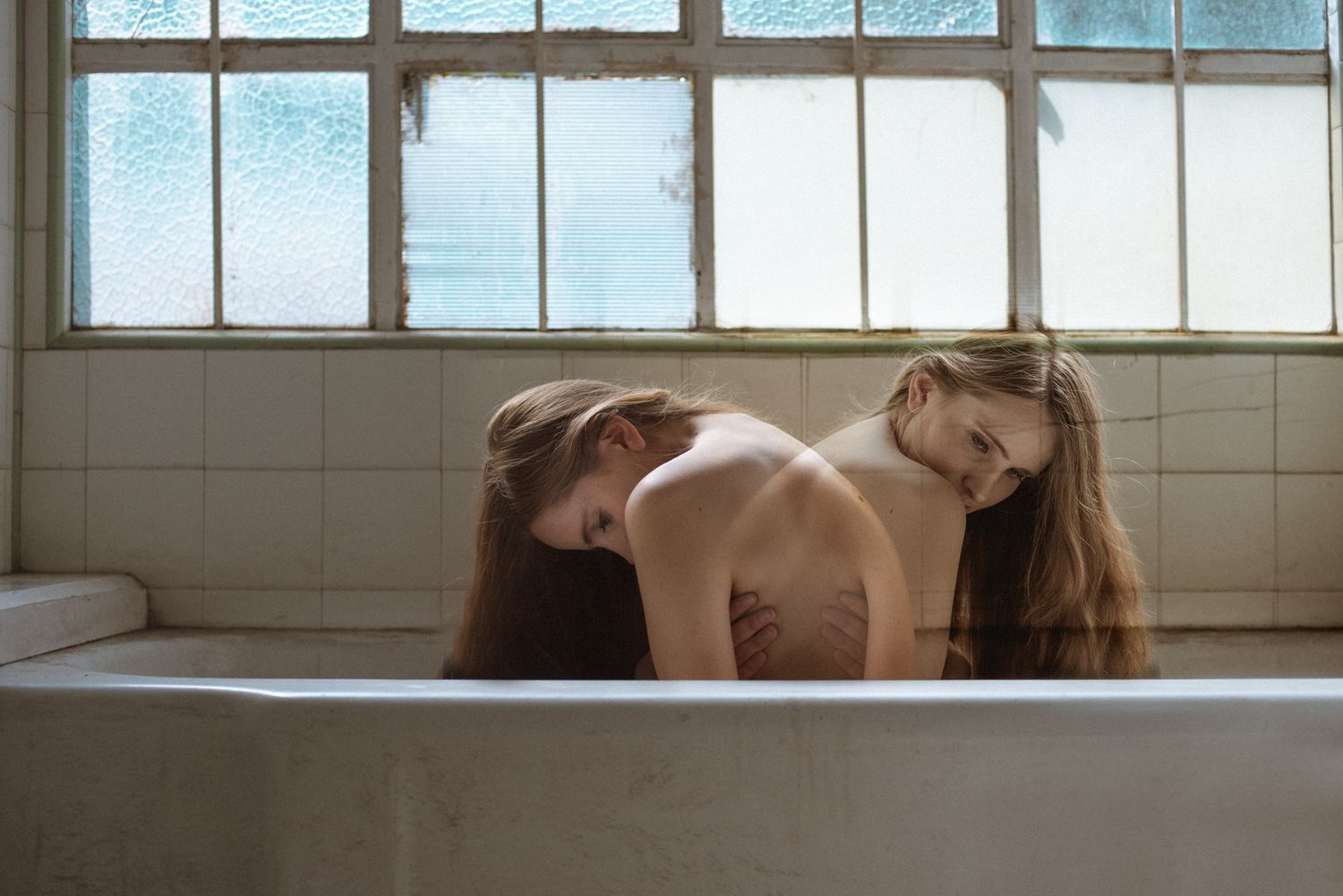 A contemplative bathtub scene with natural window lighting in an minimal interior setting.