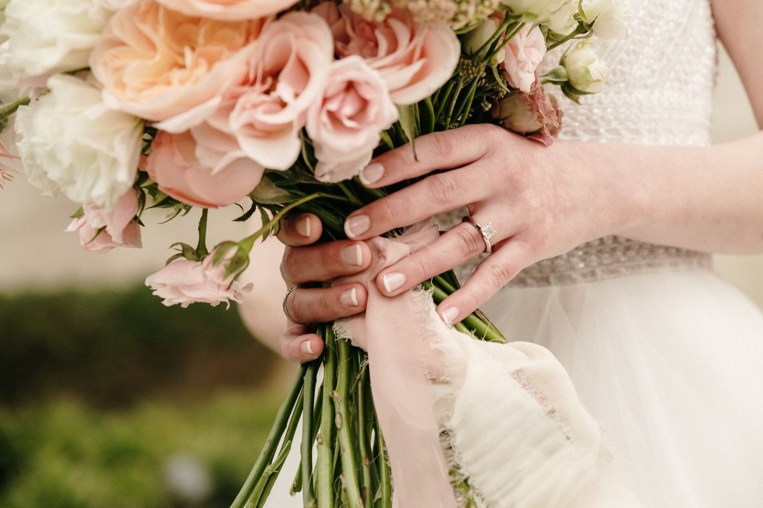 Close-up of hands holding a pink and white rose bouquet with wedding rings visible.