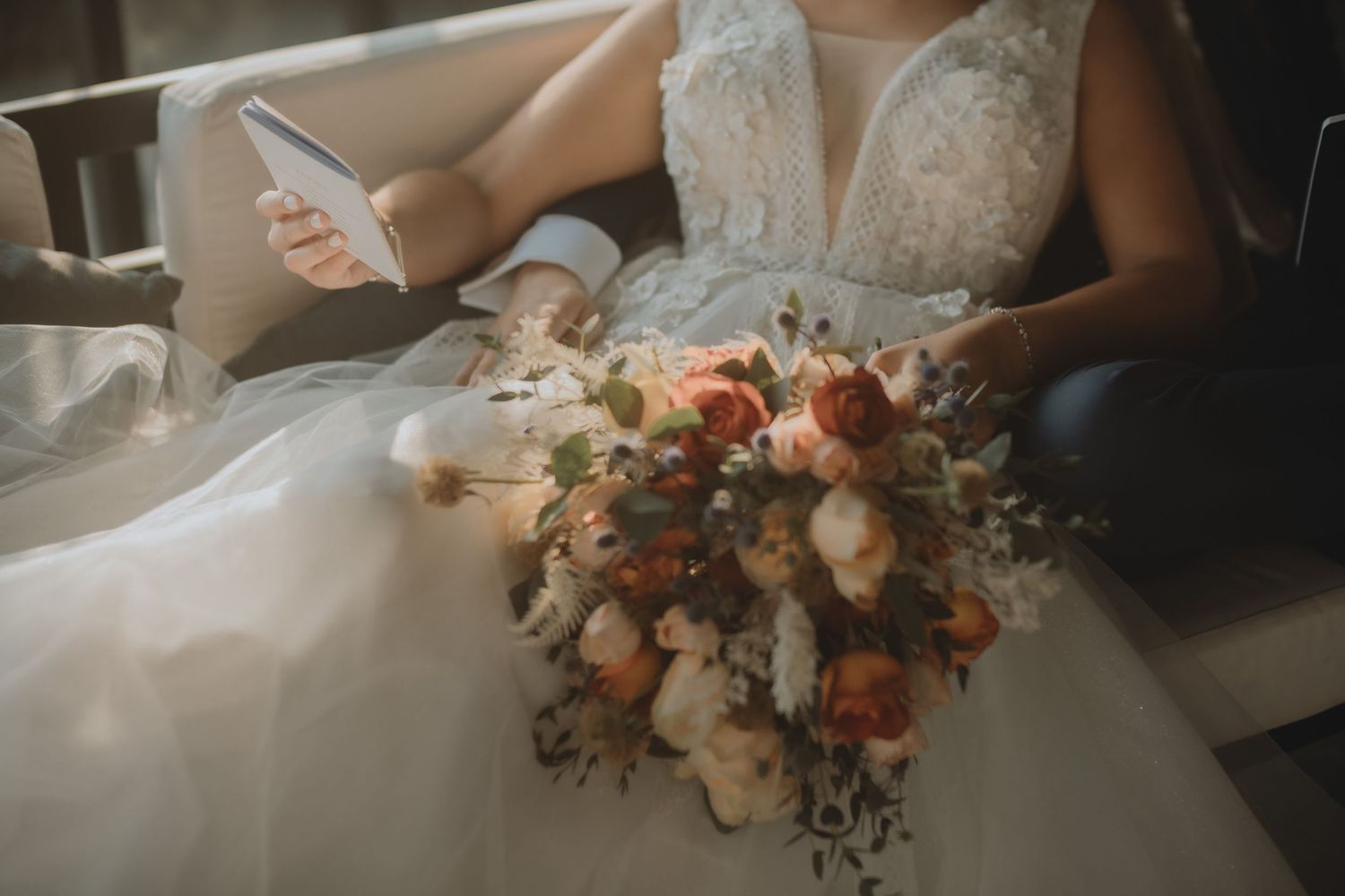 Close-up of a peach and white floral wedding bouquet resting on a white dress.