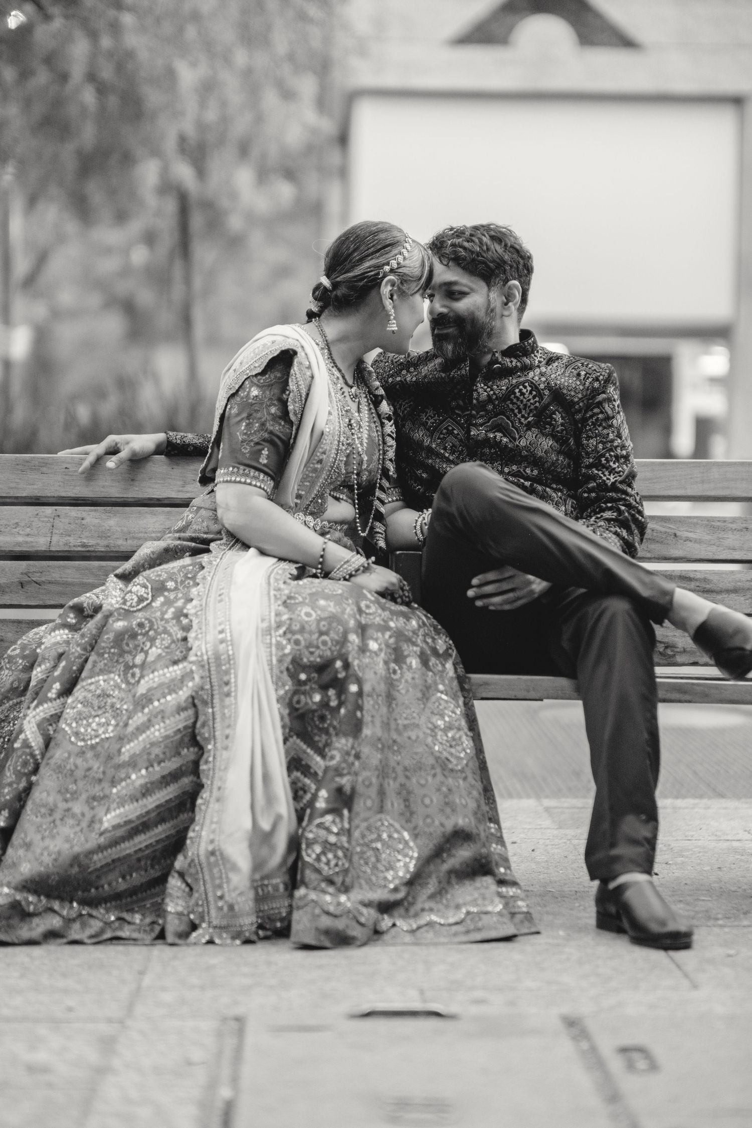 Romantic outdoor portrait of couple in traditional wedding attire sitting on bench.