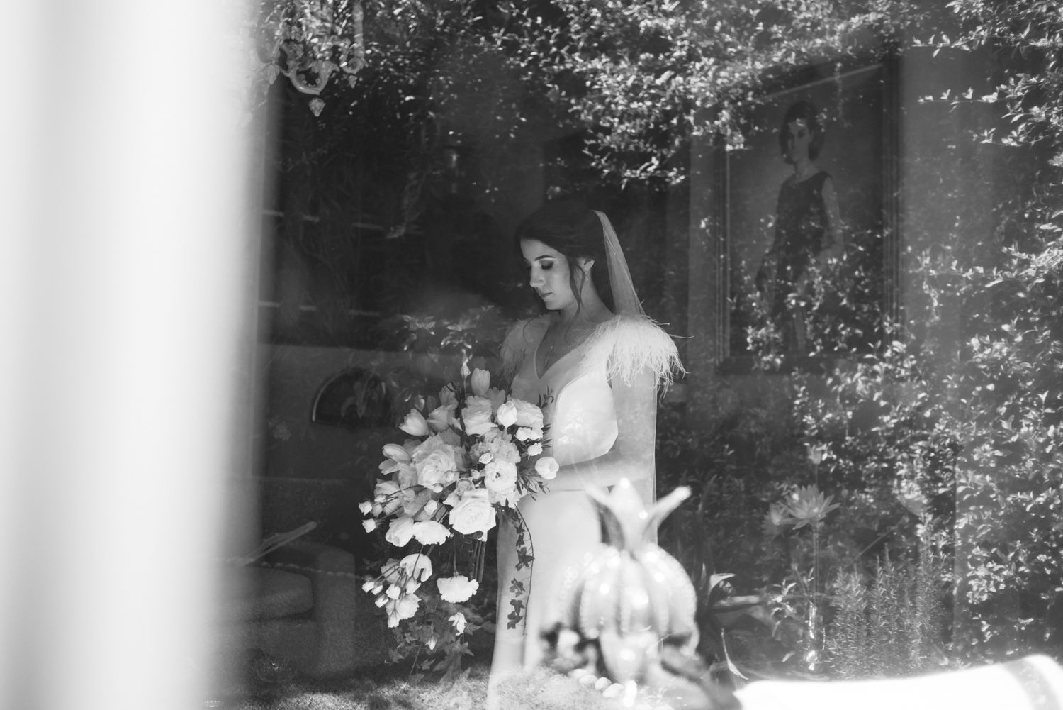 A black and white image of a bride holding a bouquet next to decorative flowers.