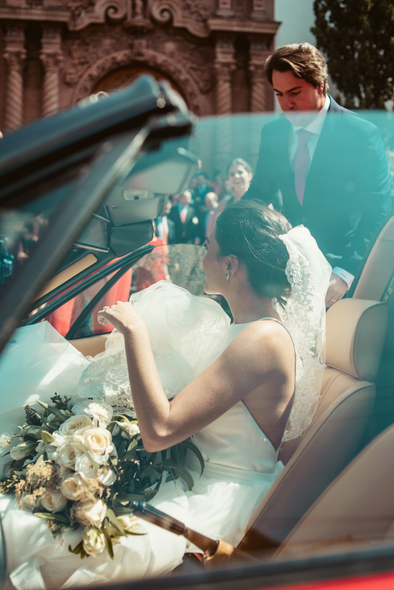 Artistic shot through convertible window of wedding couple with bouquet and decorative architecture.