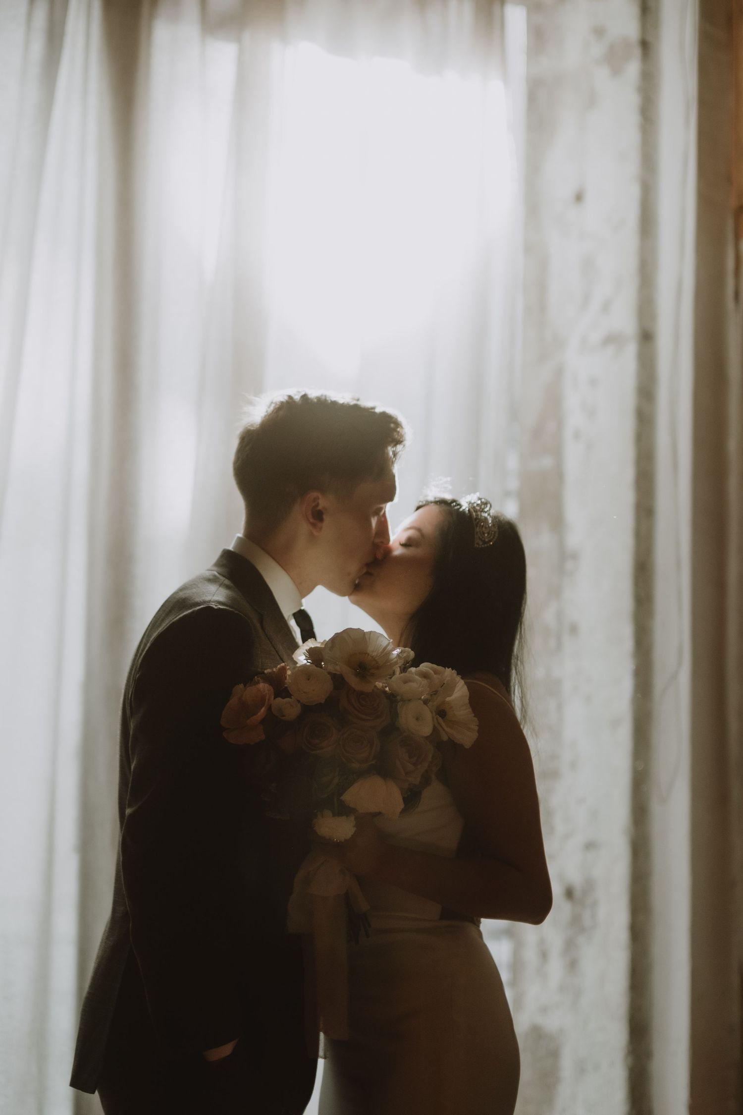 Silhouetted couple sharing an intimate moment against white curtains.