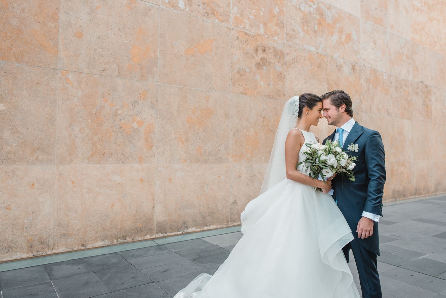 Romantic wedding portrait against a stone wall with elegant bouquet.