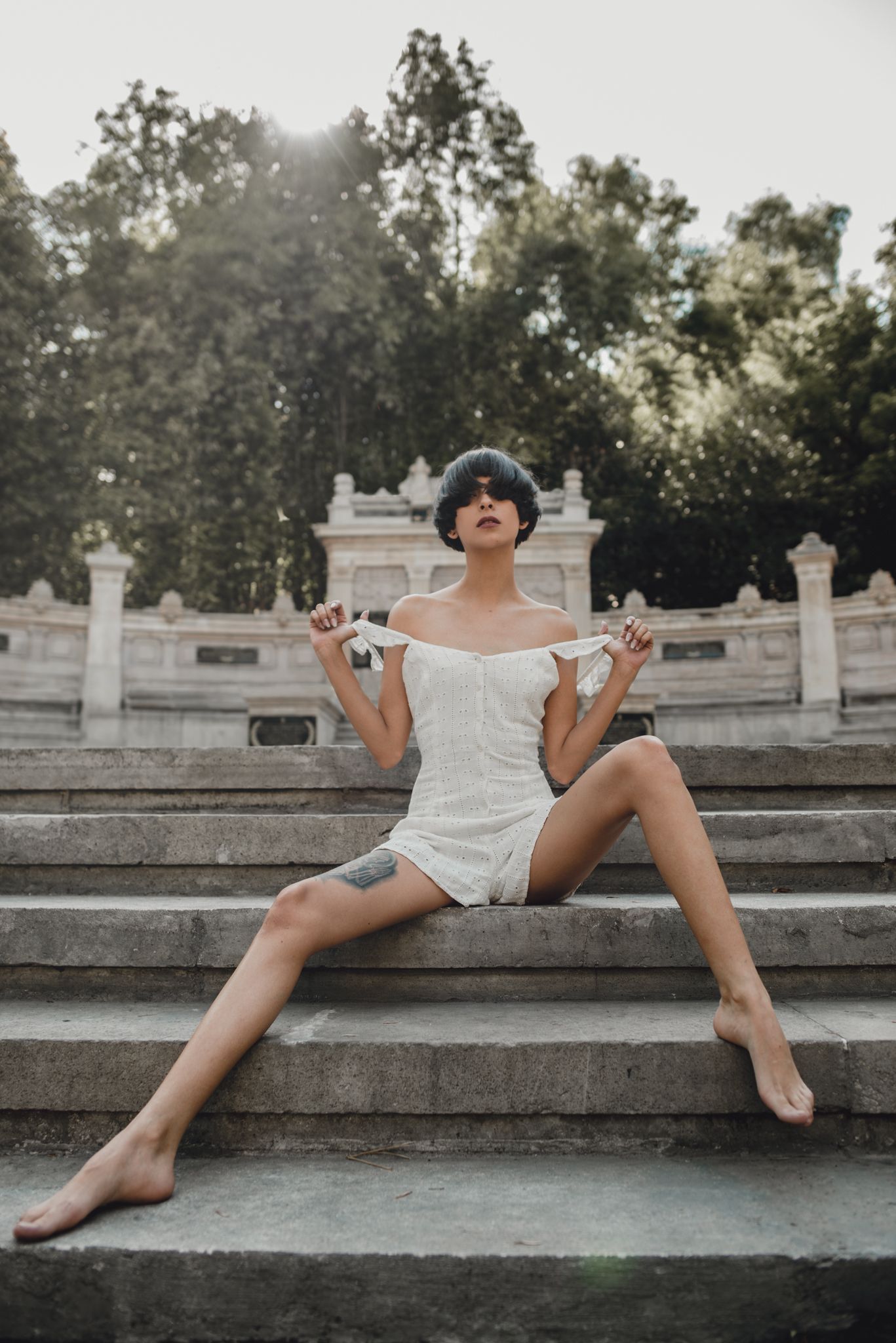 Figure in white dress poses dramatically on outdoor stone steps at sunset.