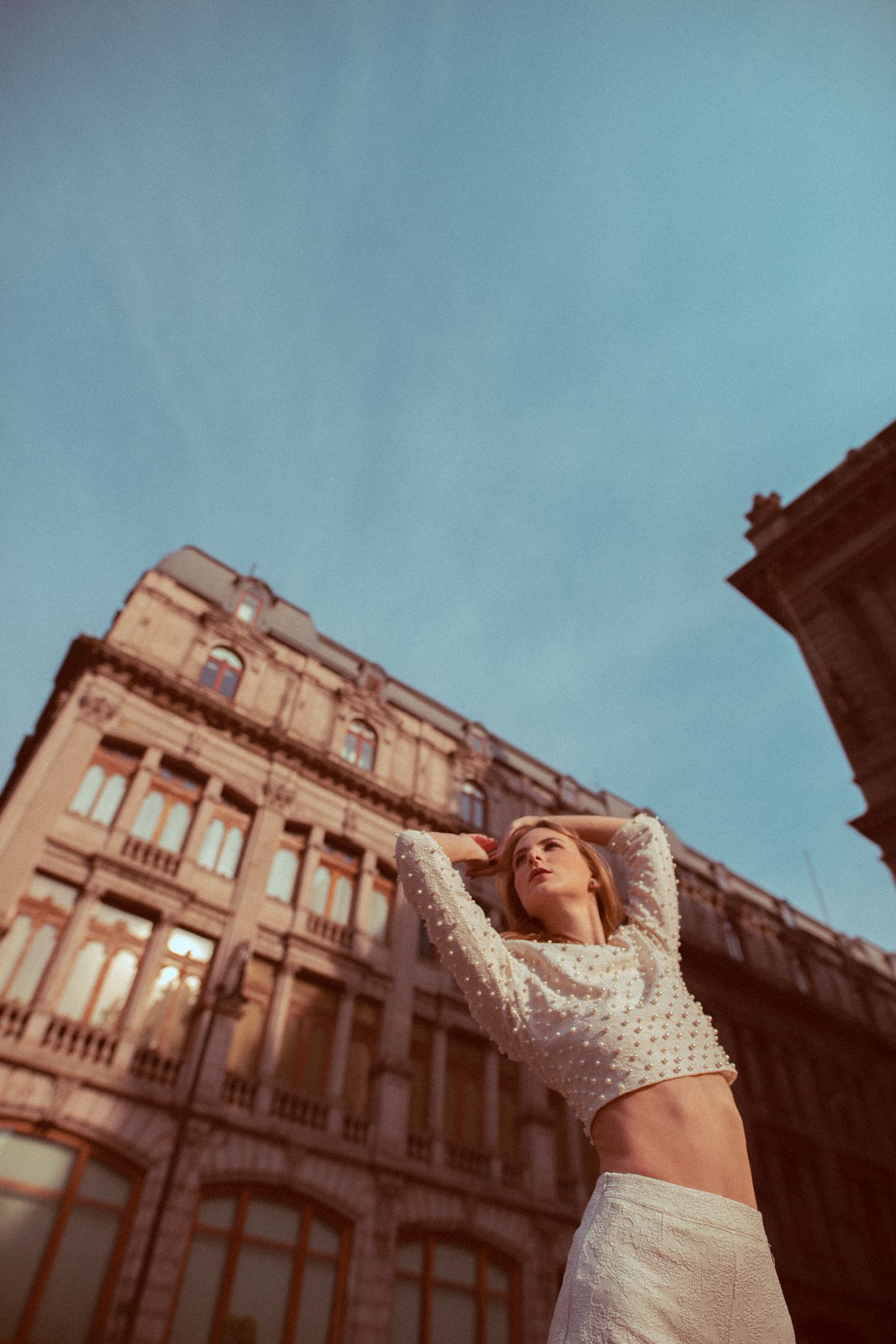 Fashion portrait of someone in white crop top posing dramatically against historic architecture.