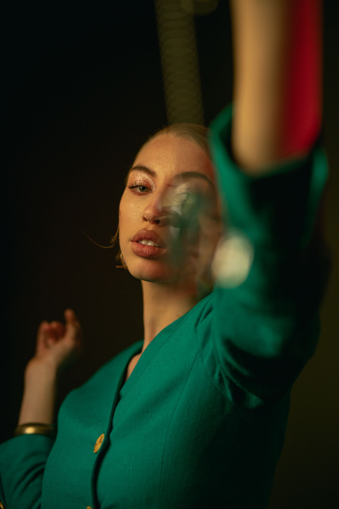 Person in emerald green blazer poses with artistic lighting and smoky atmosphere.