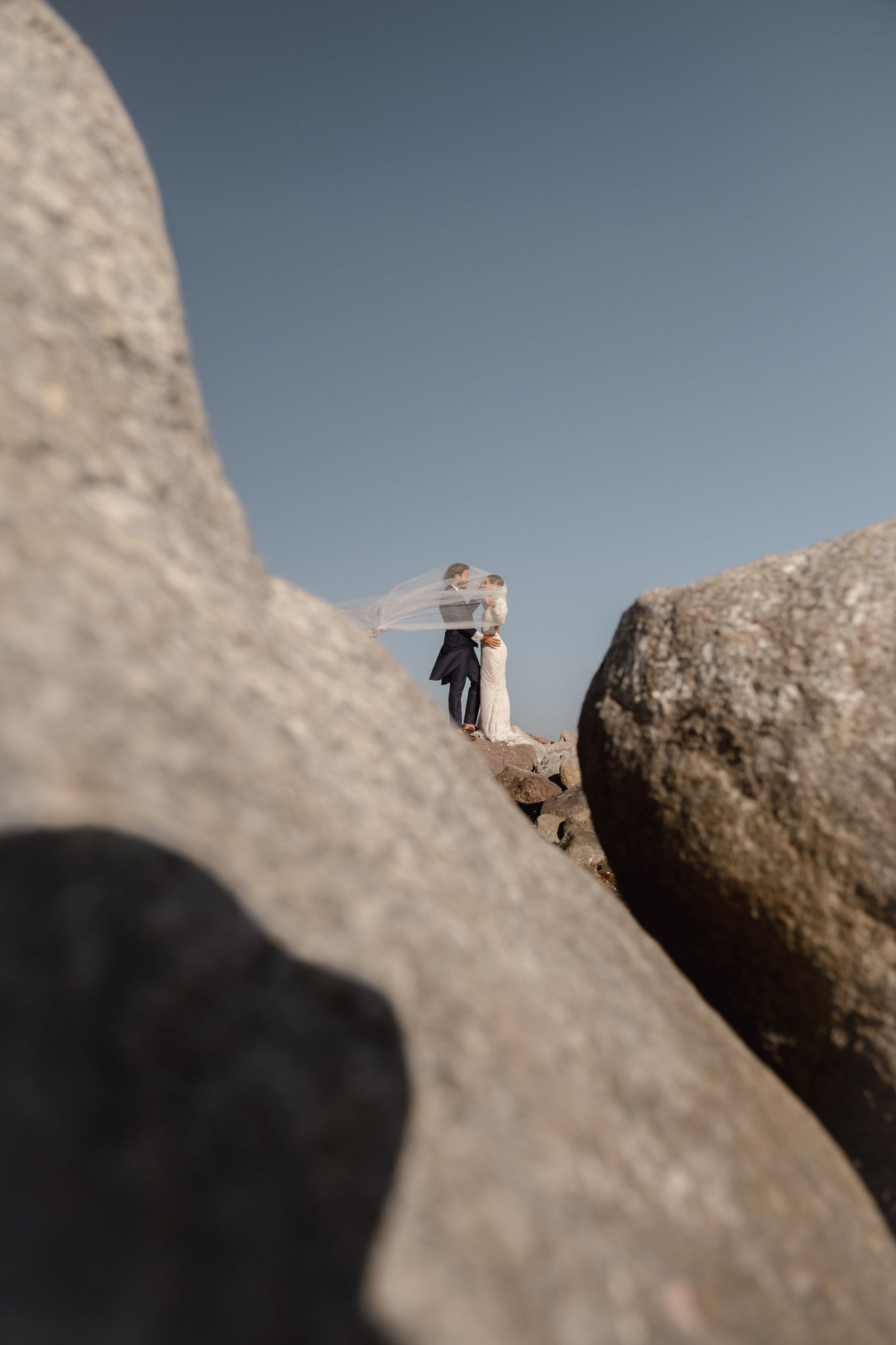 Creative angle shot of newlyweds standing among large coastal rocks.