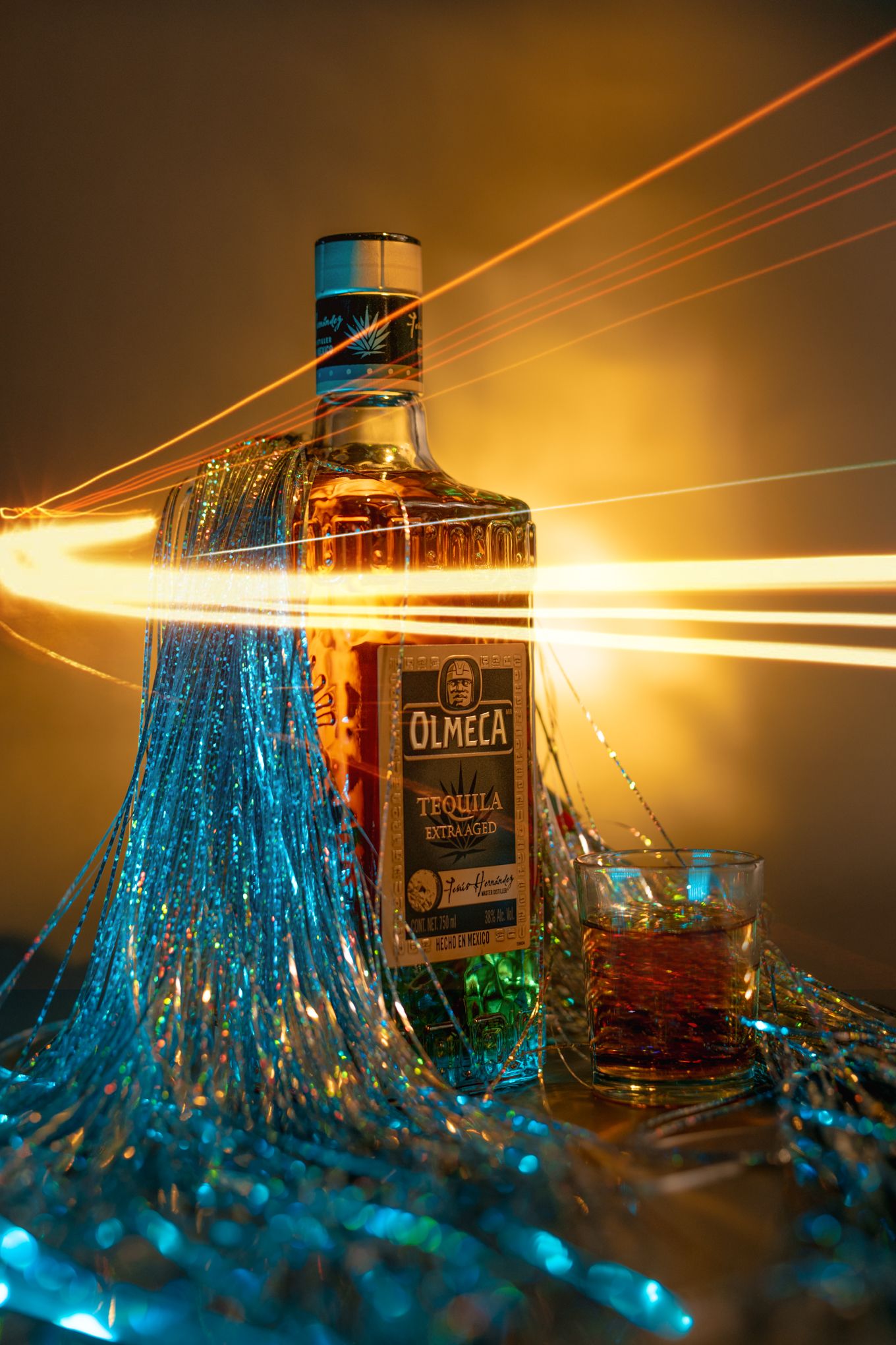 Olmeca tequila bottle with light trails and blue illumination in dramatic product photography.