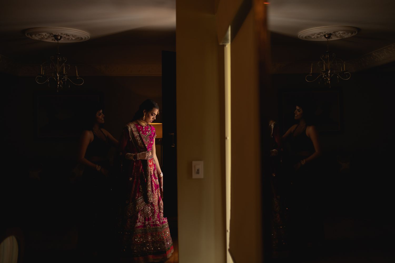 A figure in a floral maxi dress stands in a dimly lit room with a dramatic shadow cast on the wall.