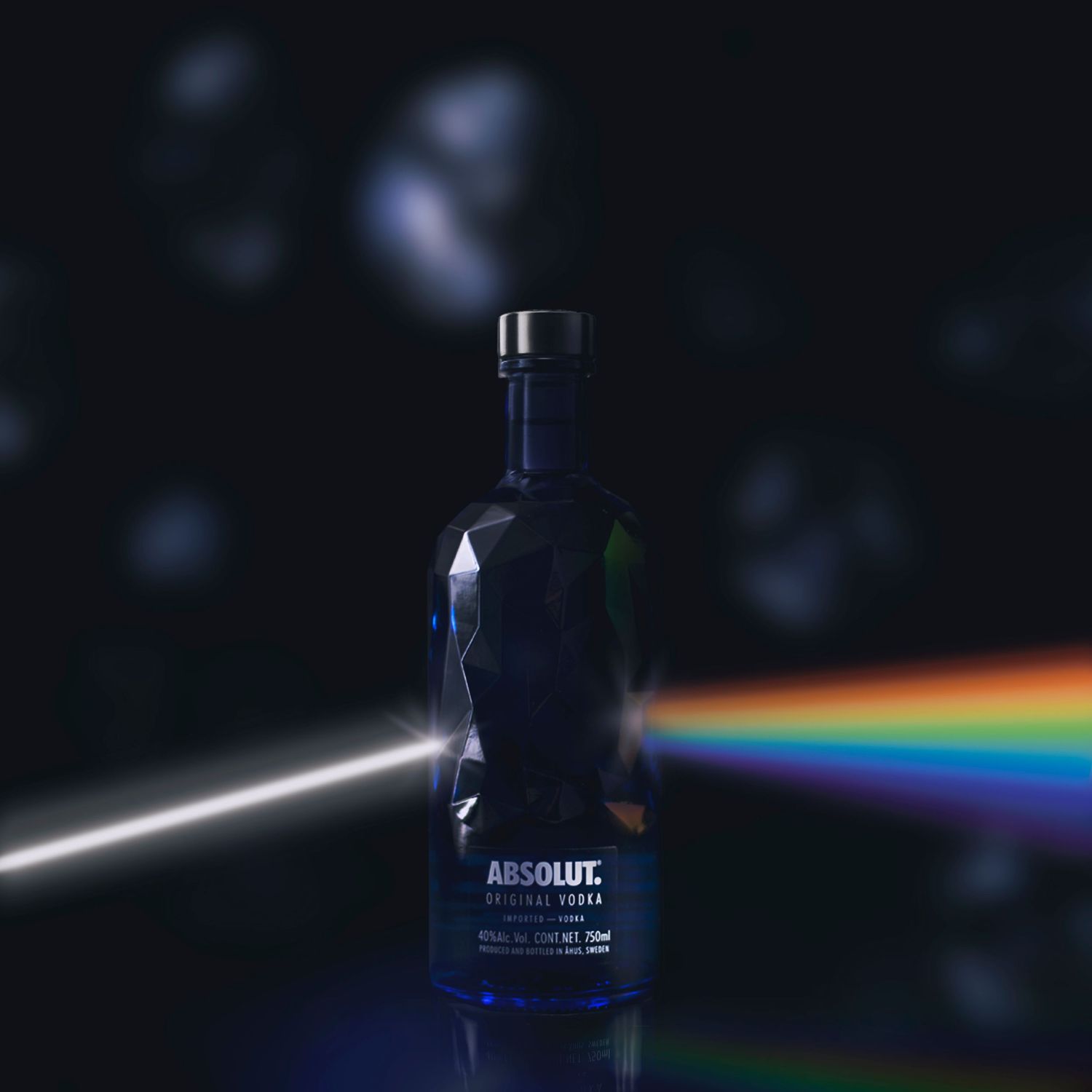 Absolut vodka bottle photographed with dramatic lighting creates a rainbow prism effect against dark background.