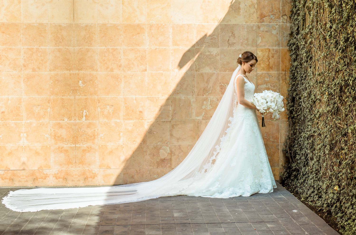A wedding dress with long flowing train photographed against a textured stone wall with elegant side lighting.