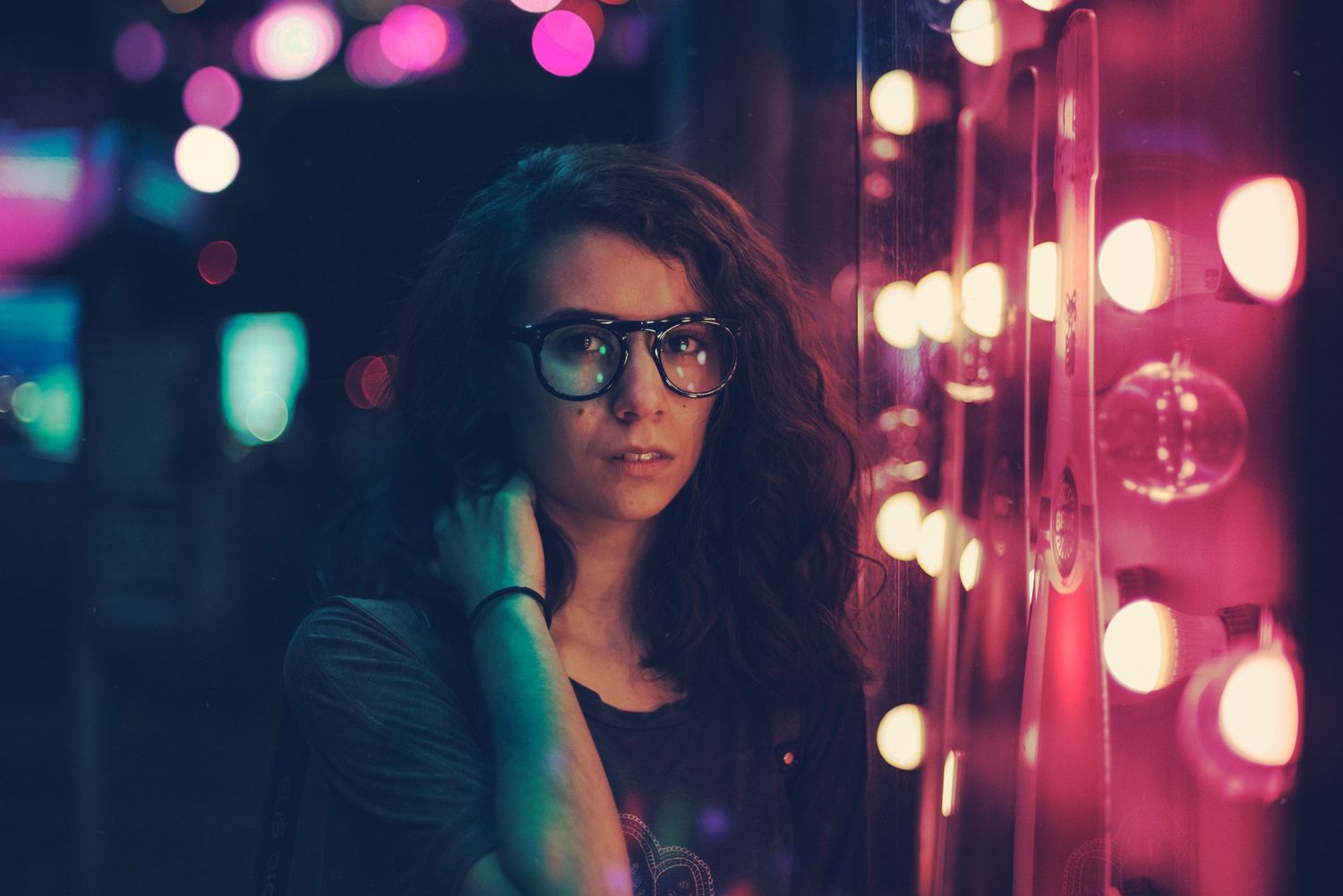 A moody portrait with glasses framed by pink and purple bokeh lights in an atmospheric nighttime setting.