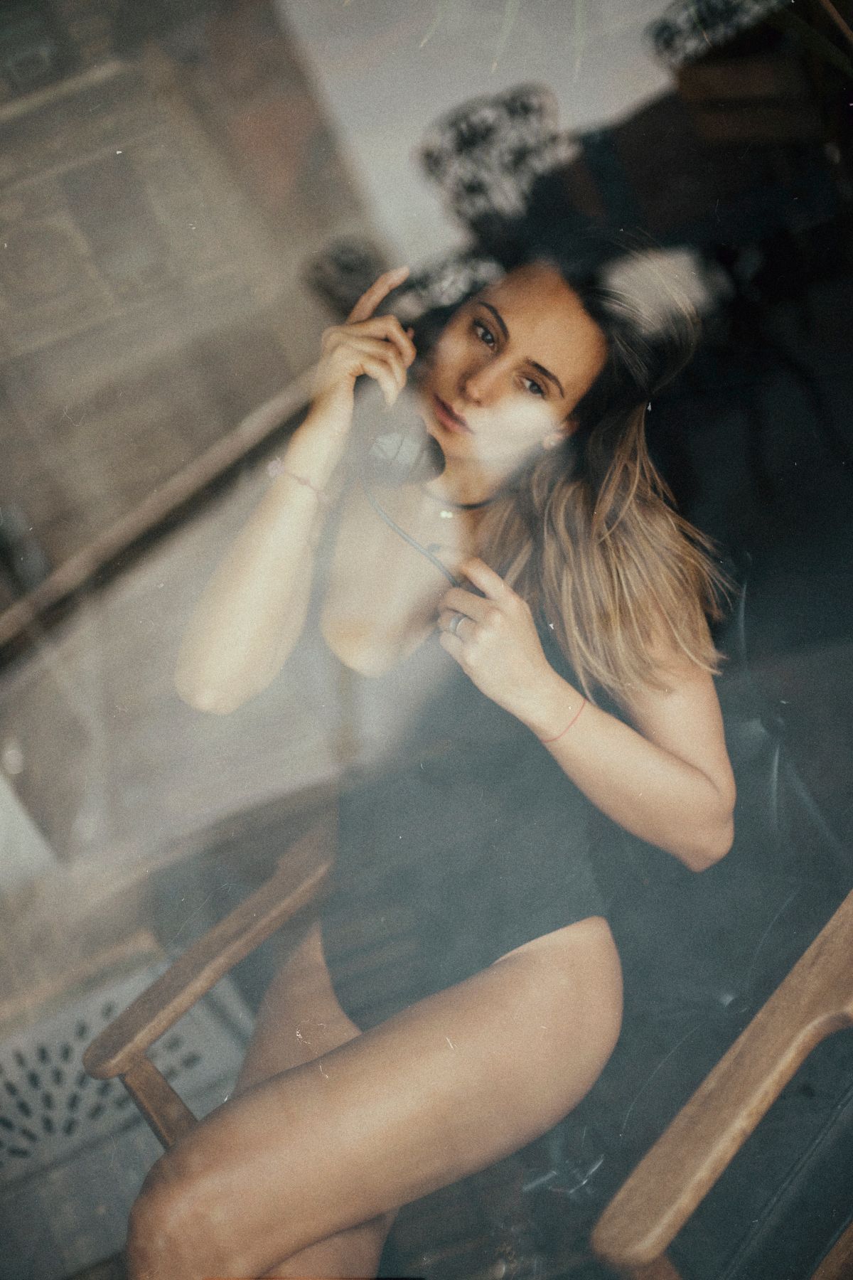 Artistic boudoir portrait through glass with moody lighting and reflections.