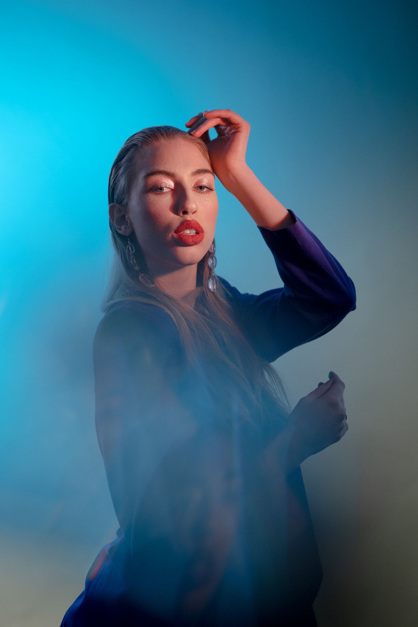 Artistic portrait in blue lighting with figure in dark clothing making dramatic pose.