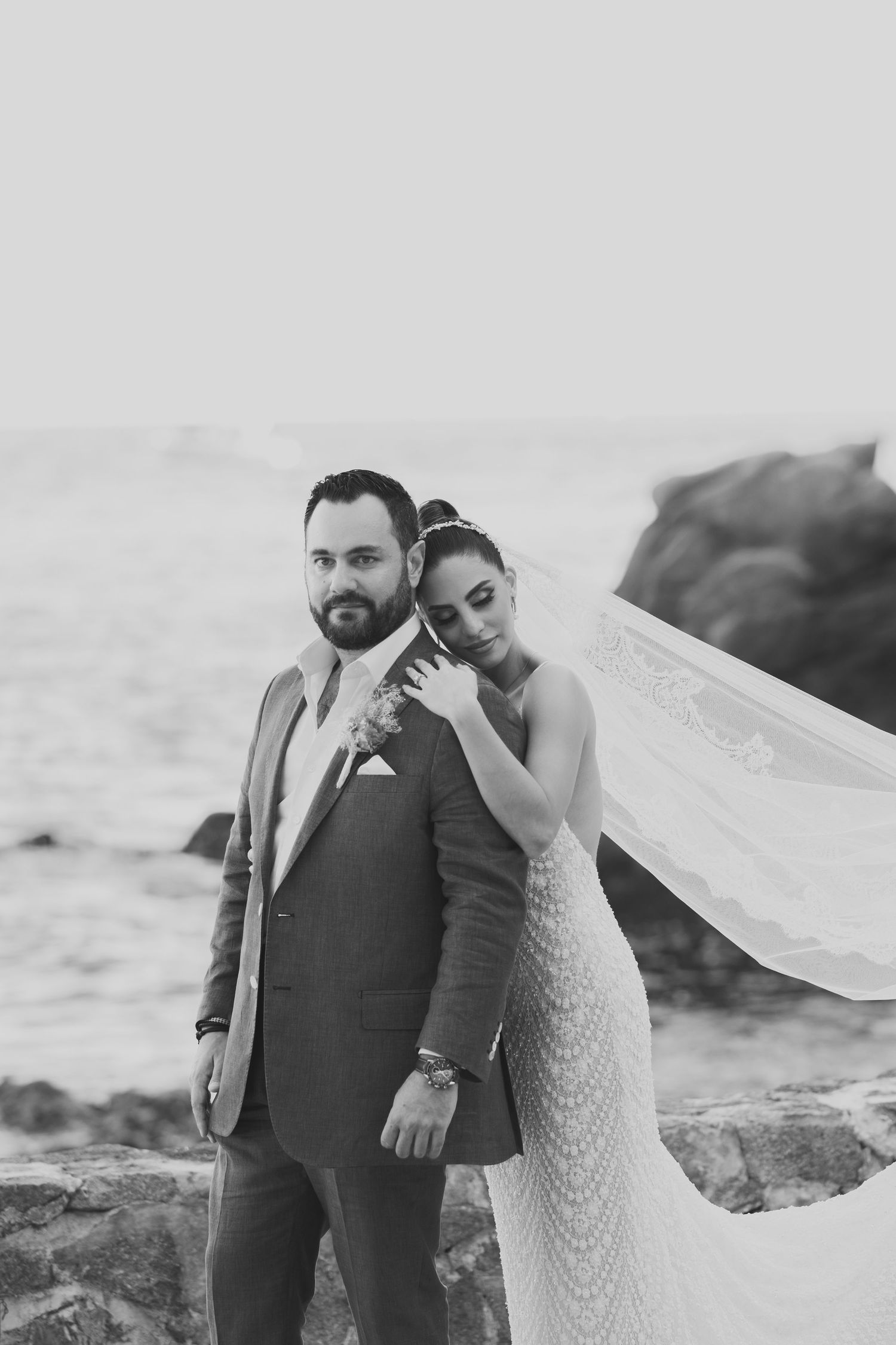 A romantic coastal wedding photo featuring a couple embracing on rocky cliffs by the ocean.