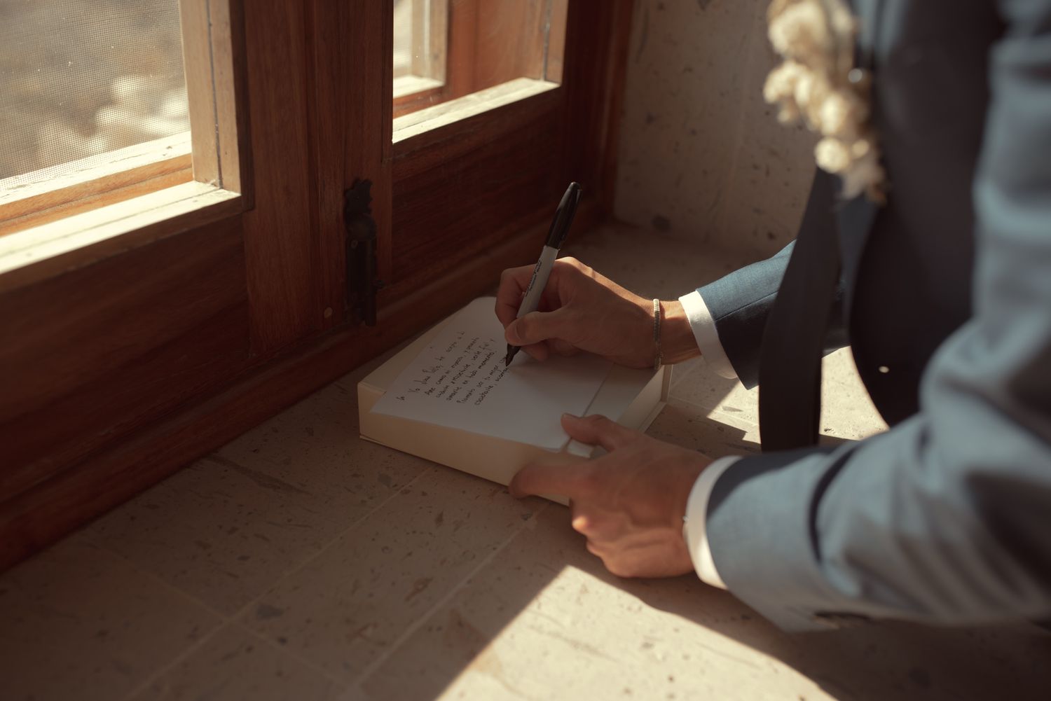 A person signing a wedding guestbook near a window with natural light streaming in.