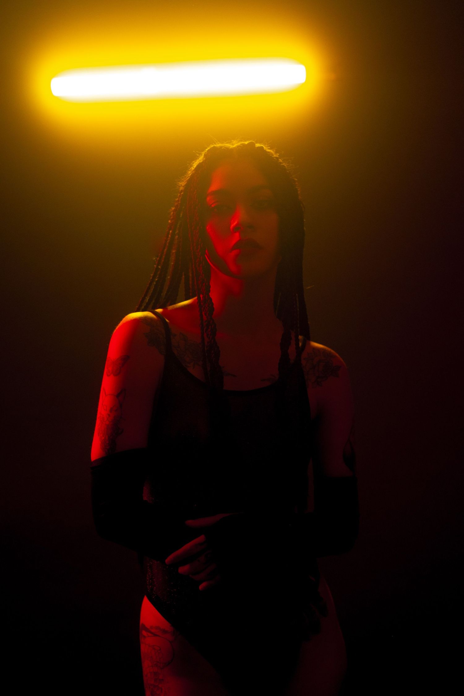 Silhouette in a black swimsuit stands beneath a glowing yellow light bar against dark background with red lighting effects.