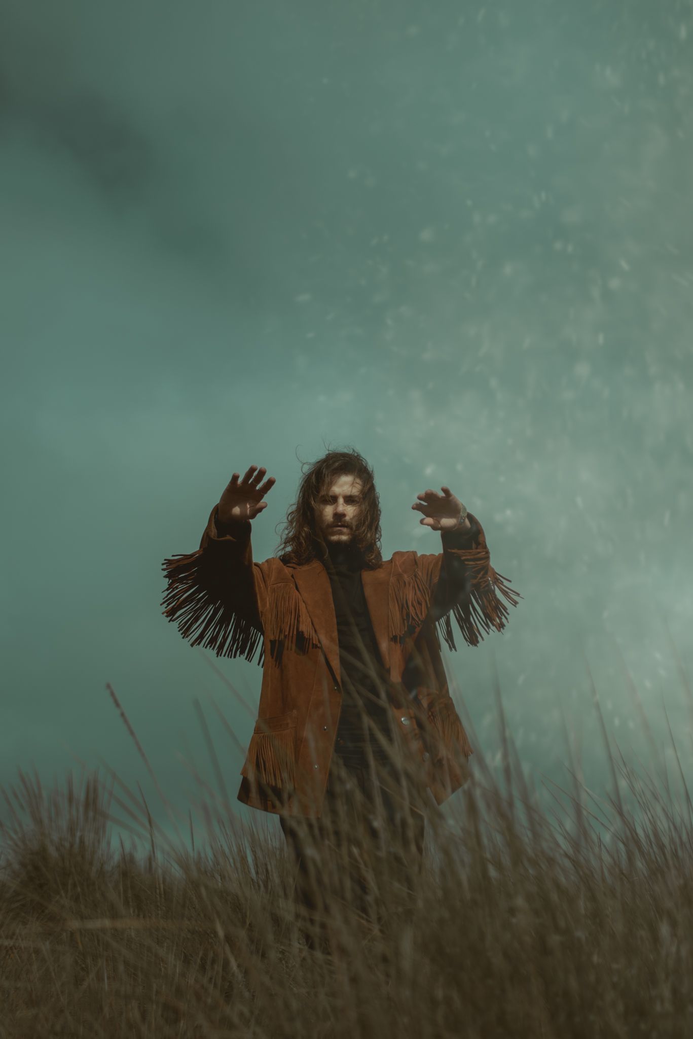 Dramatic scene of person in fringe jacket with raised arms in stormy field.