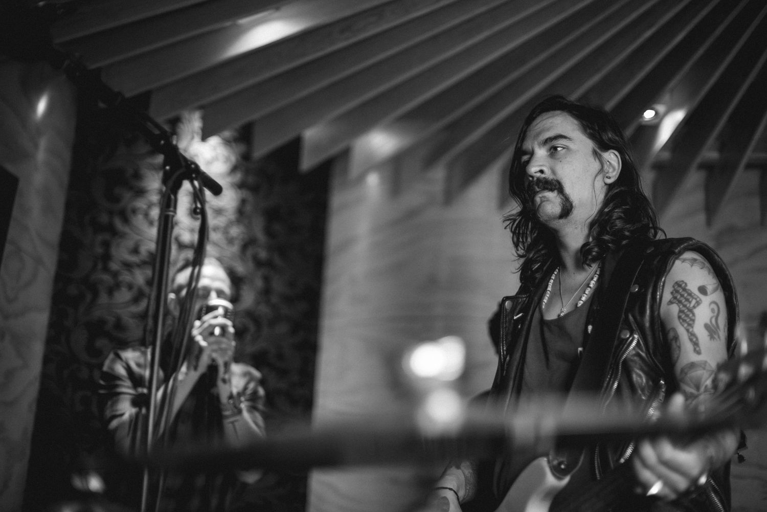 Black and white concert photo of long-haired musician performing with stage lighting effects.
