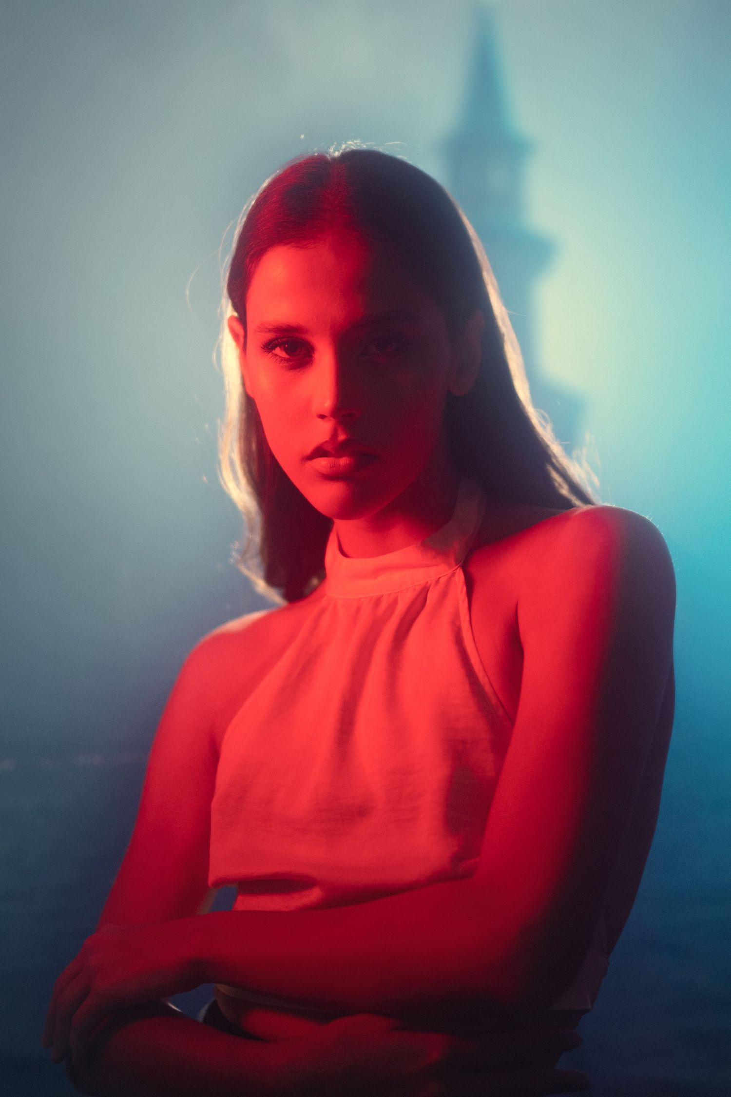 Moody portrait with red and blue lighting against hazy urban background.