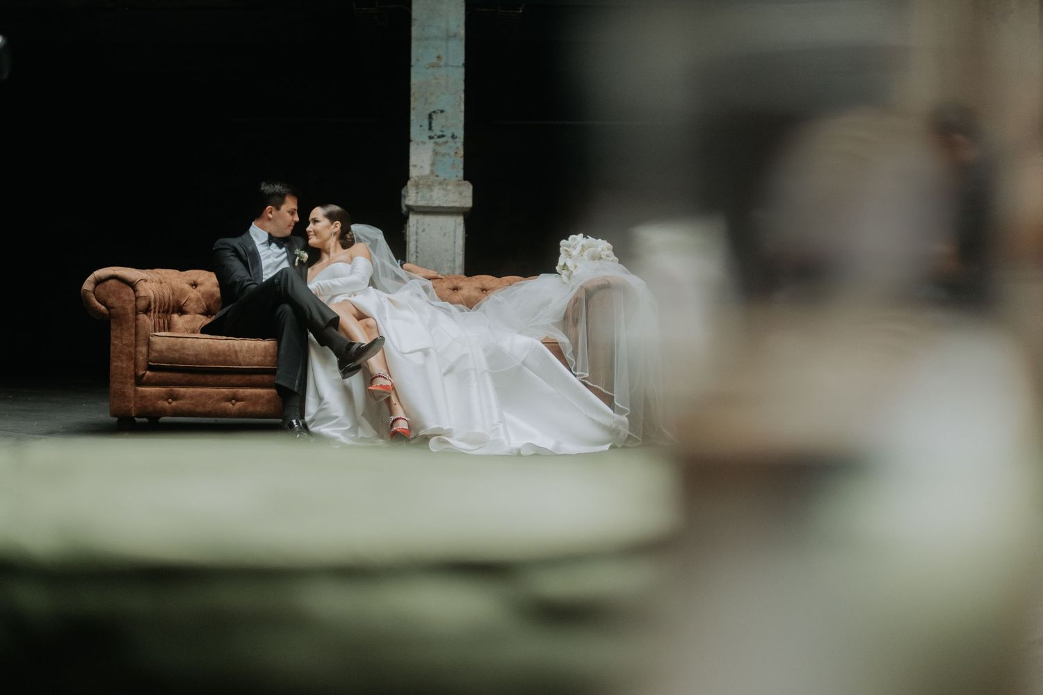 Romantic wedding couple lounges together on a vintage brown leather chair in an intimate setting.