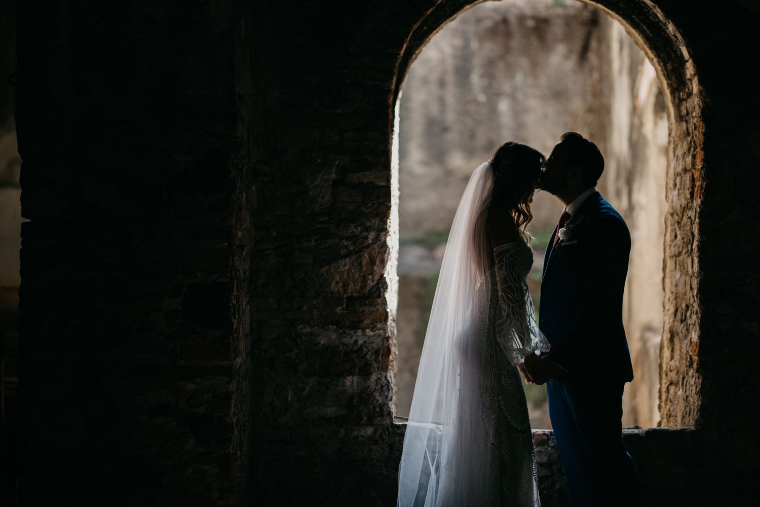 Romantic silhouette of couple embracing in historic stone archway.