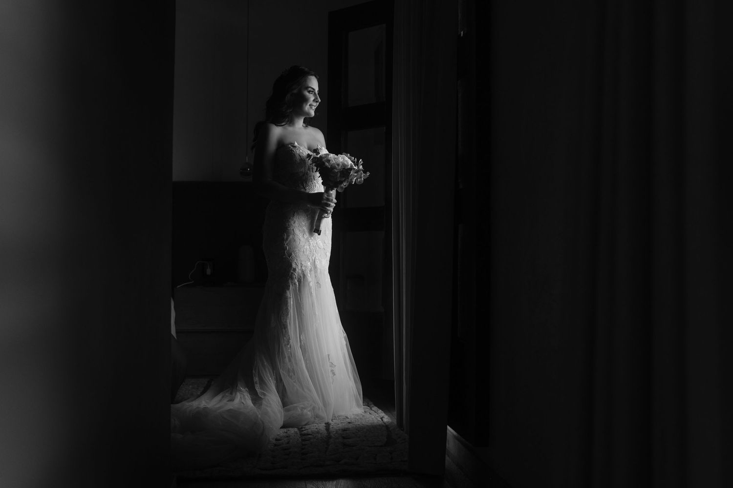Black and white photo of a wedding dress framed dramatically through a doorway.