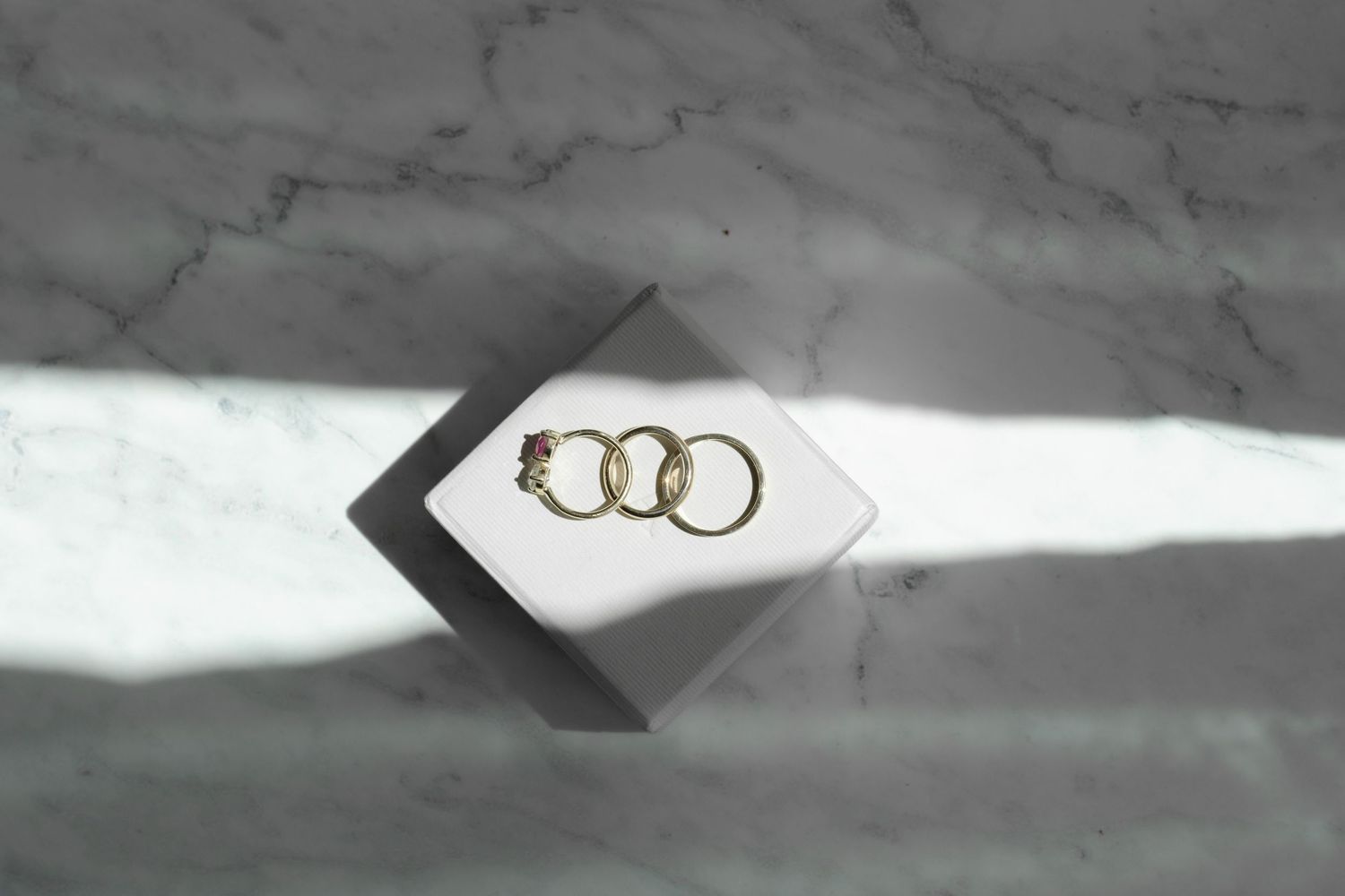 Three wedding rings arranged artistically on geometric marble surface.