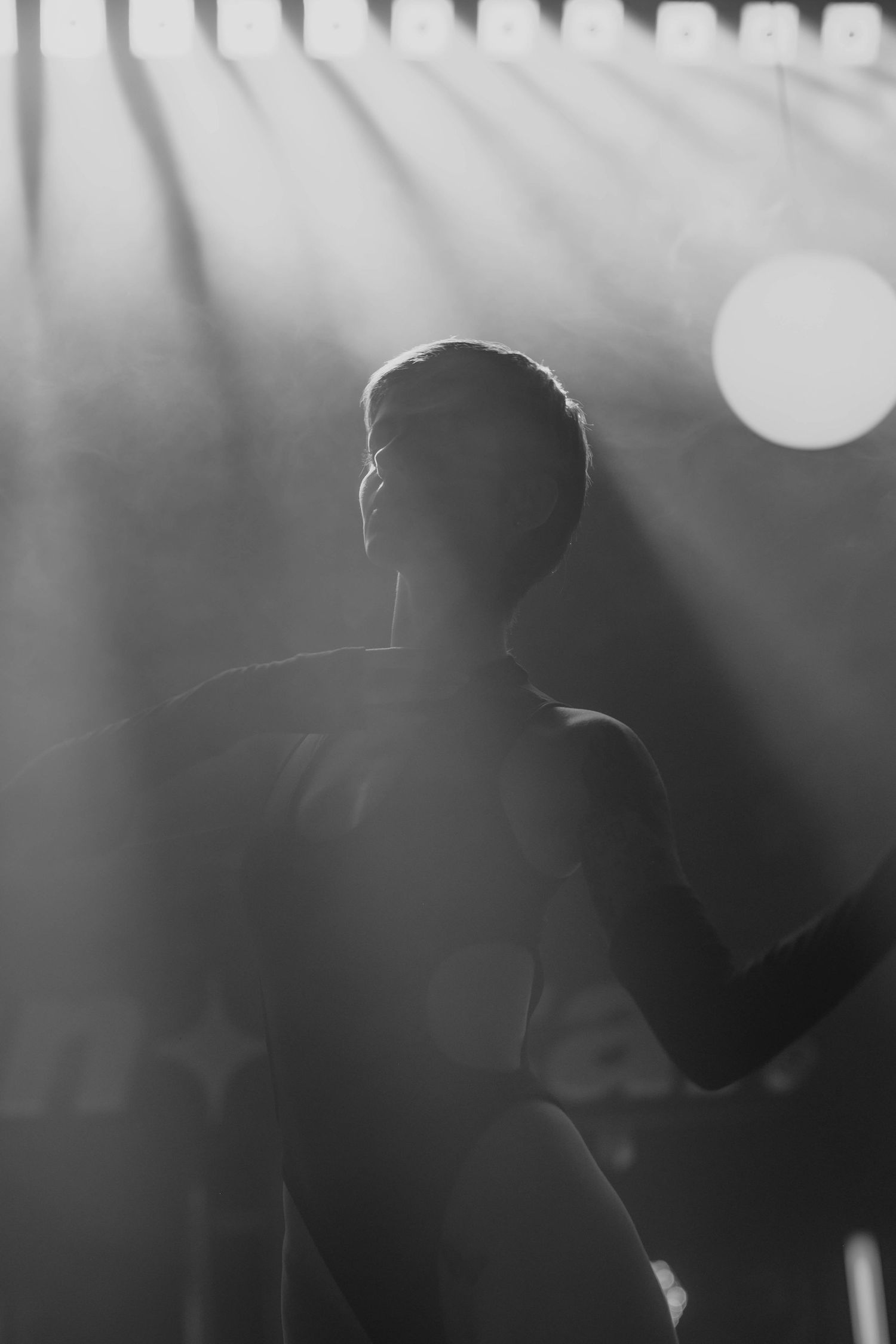 Black and white silhouette of performer under dramatic stage lighting.