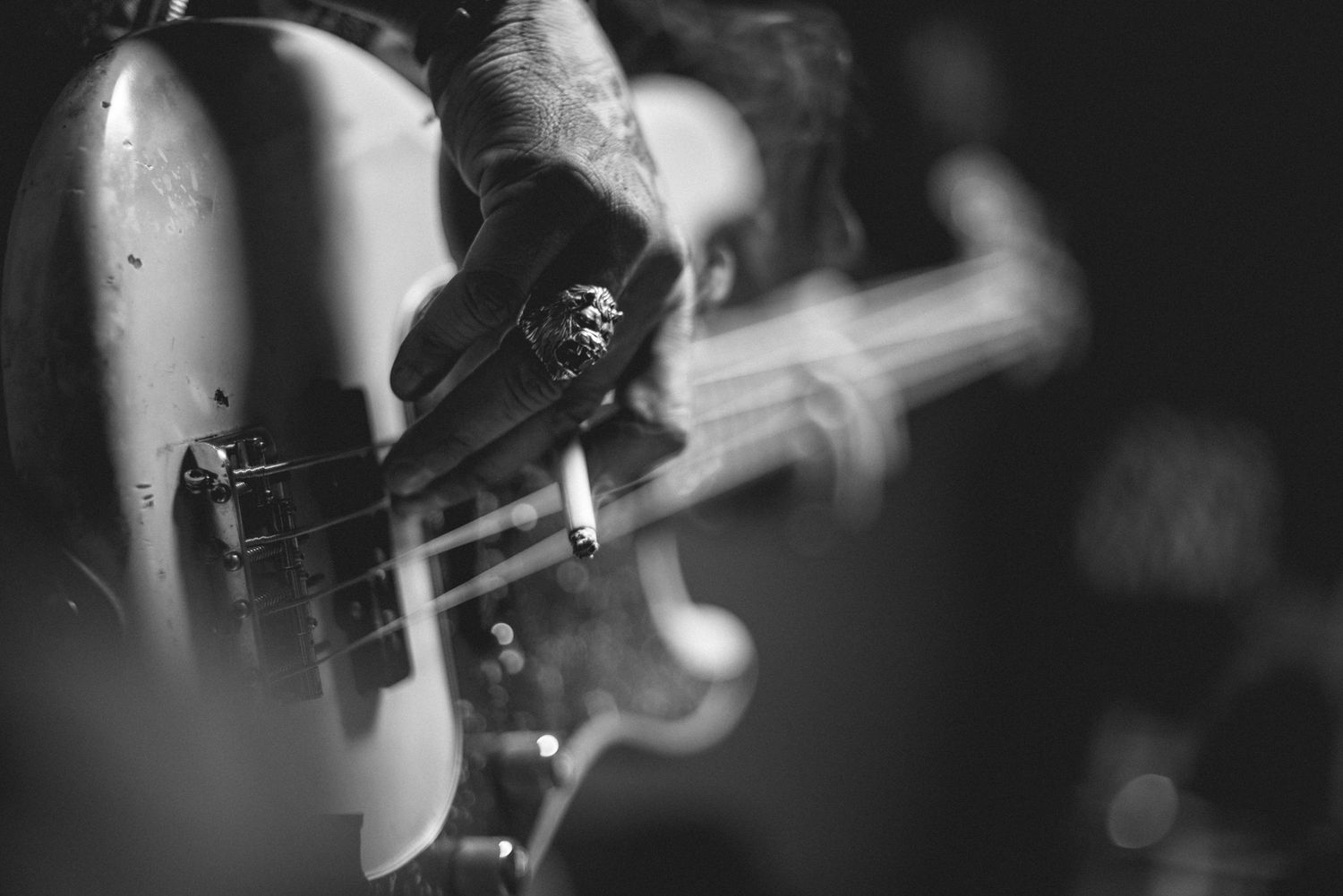 Close-up black and white shot of hands playing bass guitar with shallow depth of field.