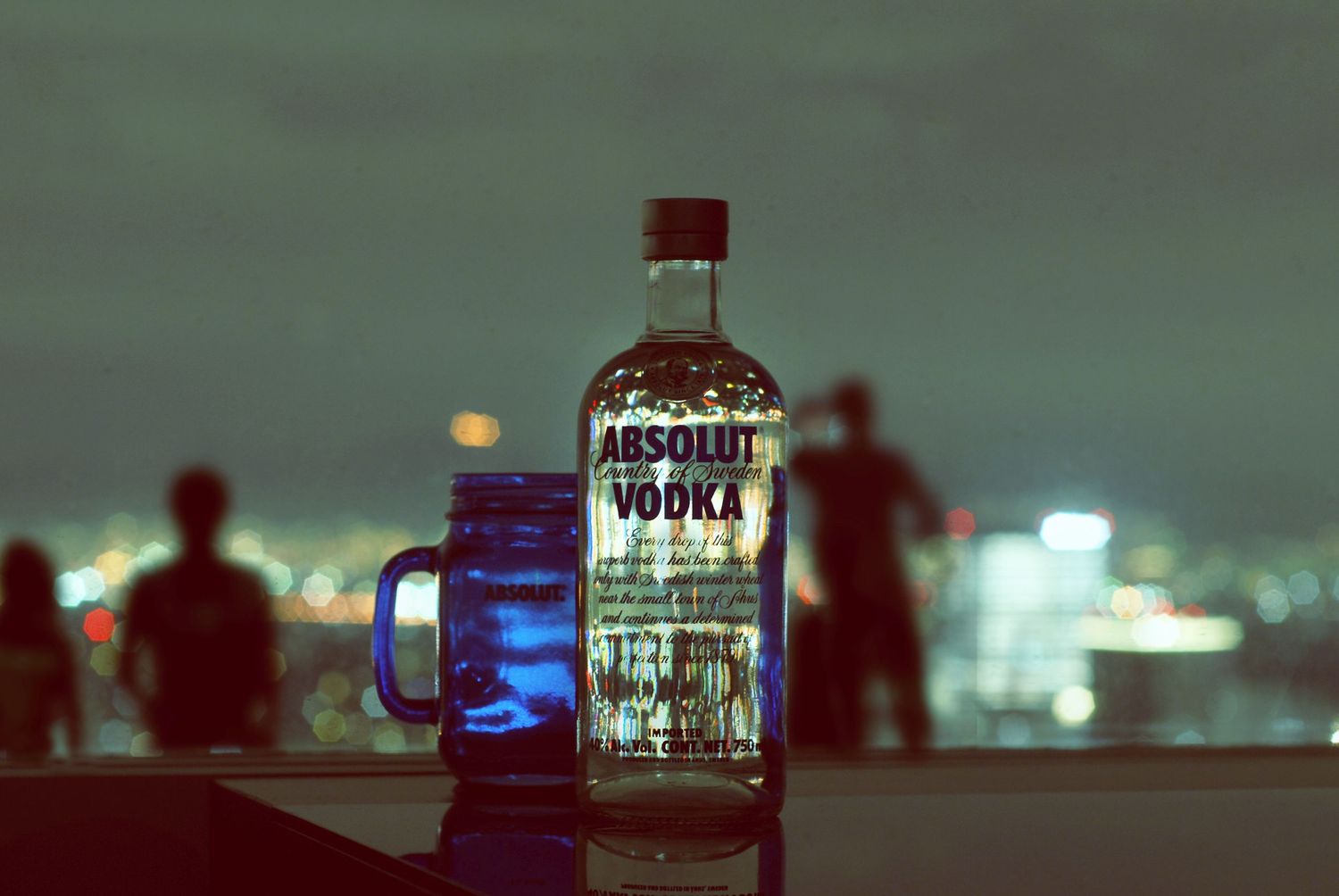 Illuminated row of liquor bottles on a bar shelf with glowing lights creating an atmospheric nighttime ambiance.