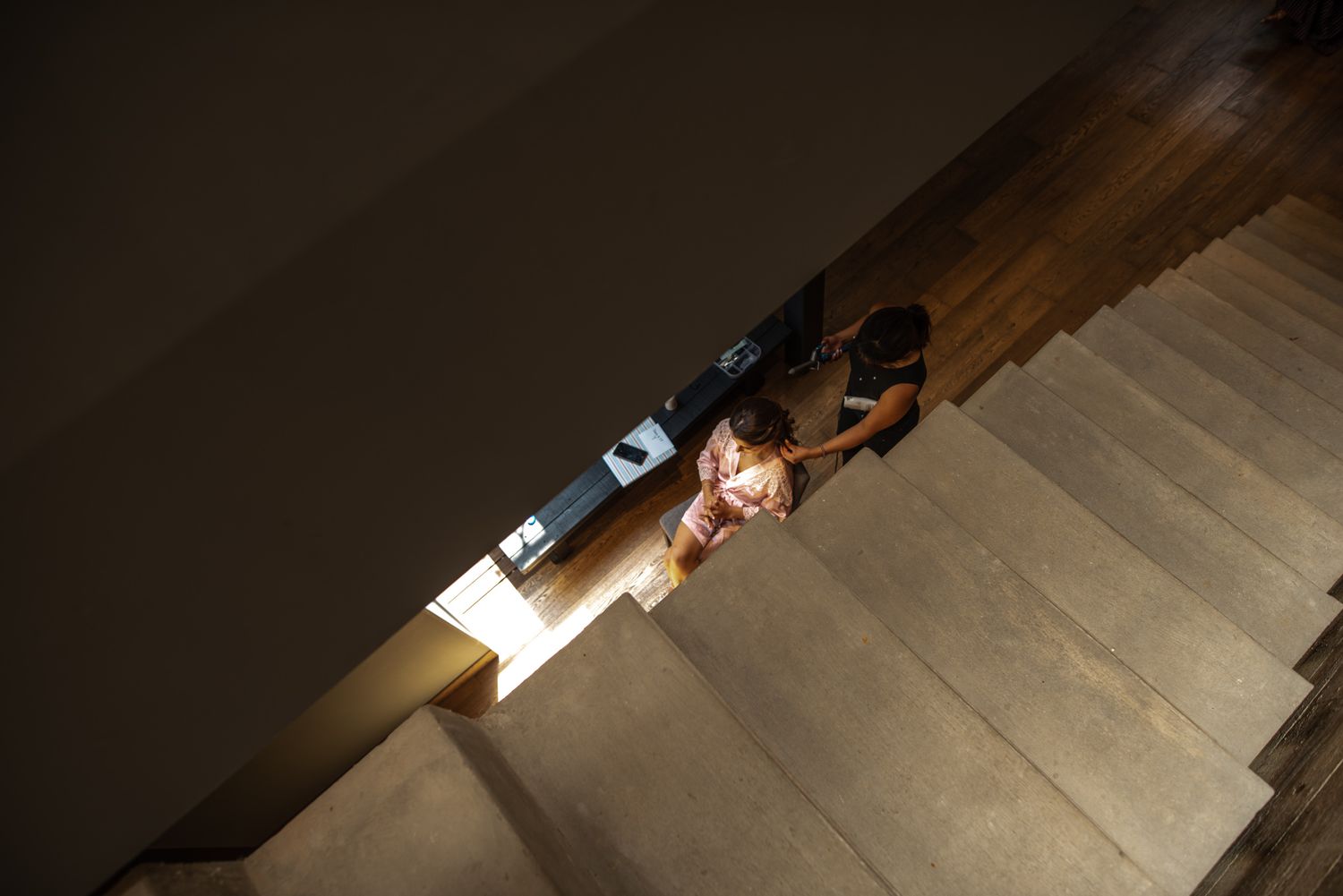 Someone lies on concrete stairs illuminated by dramatic overhead lighting, creating strong shadows and contrast.