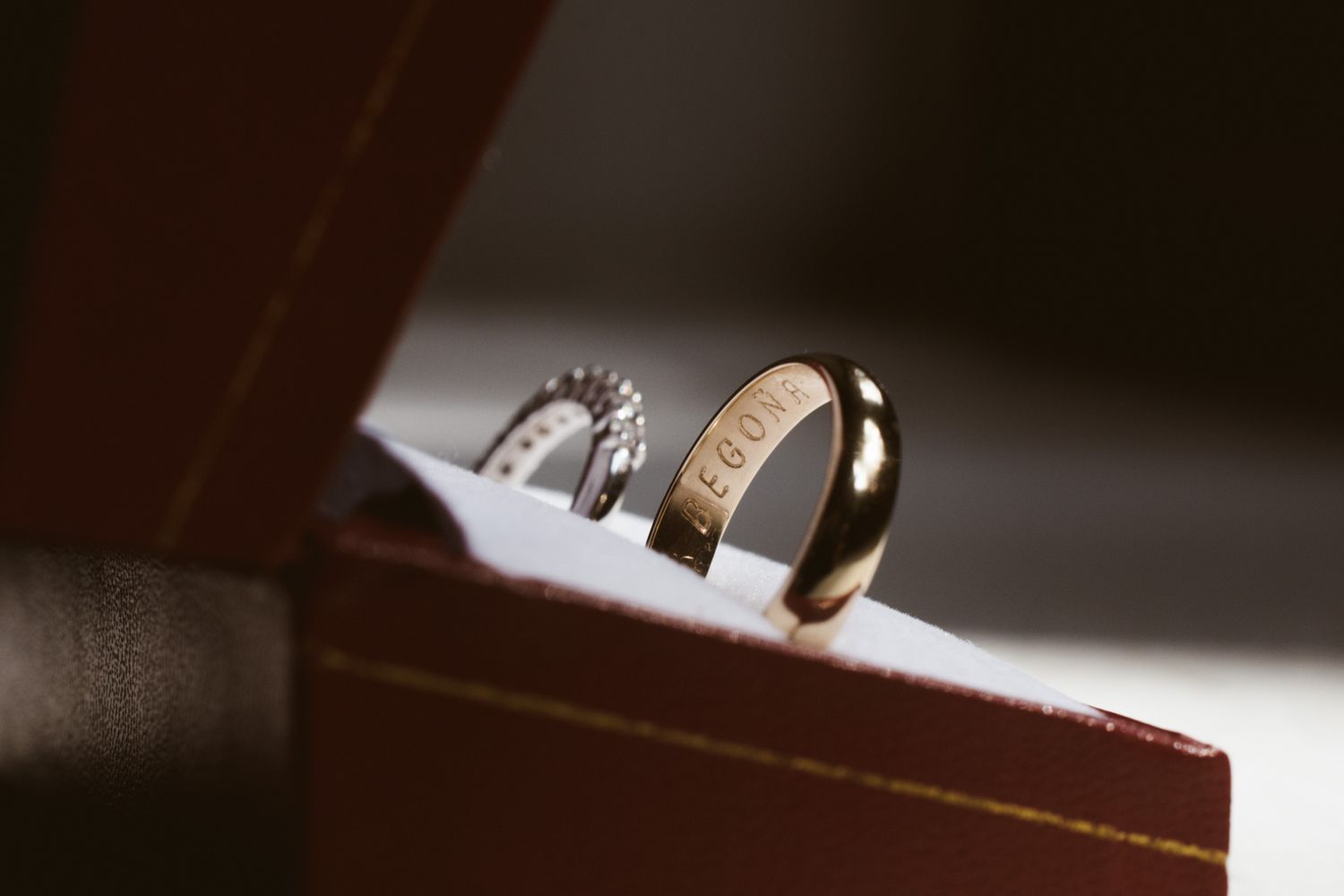 Two elegant wedding rings rest on the edge of a leather box with one band featuring a shiny metallic finish.