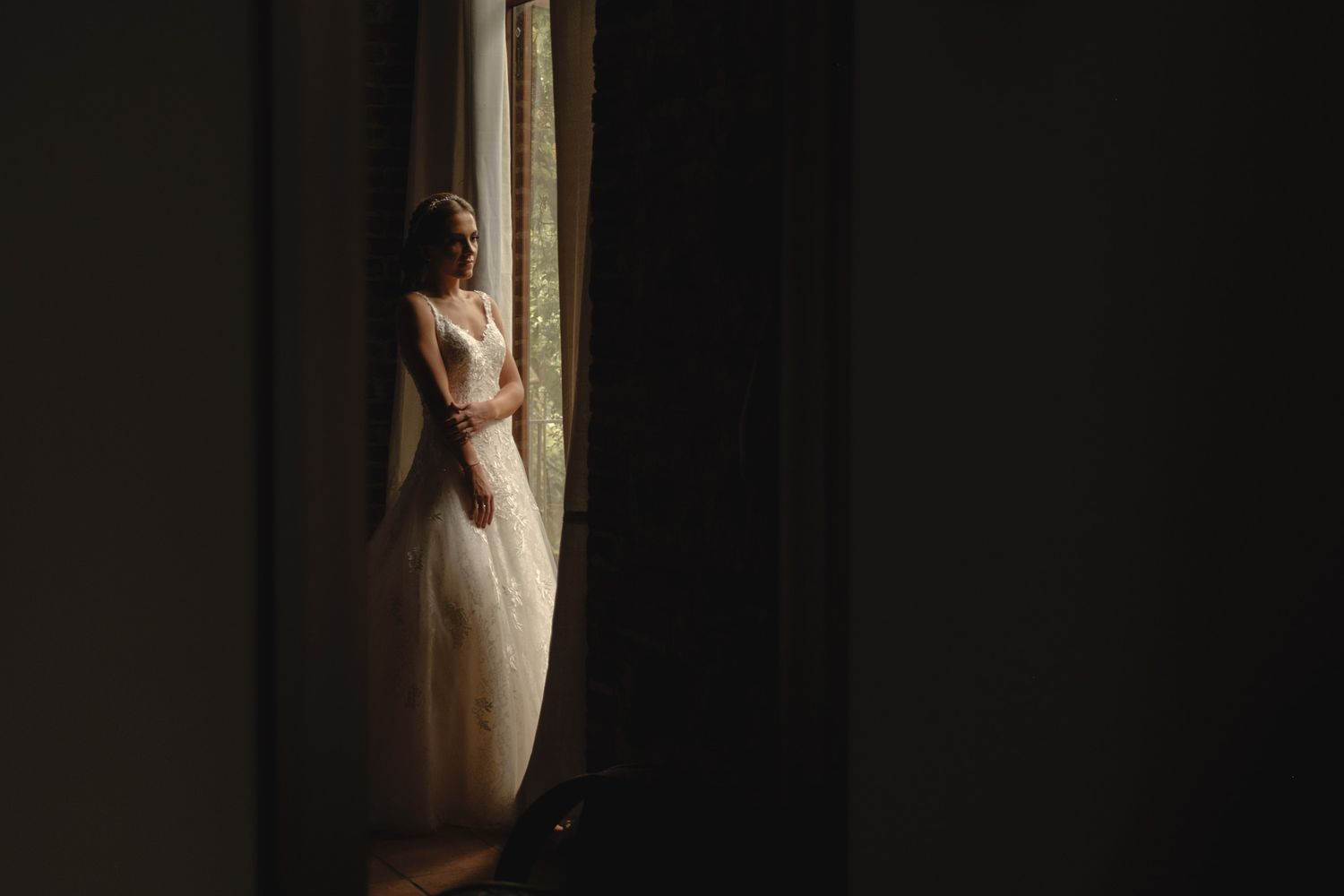 A silhouetted figure in a wedding dress stands in dramatic window light creating a moody, artistic composition.